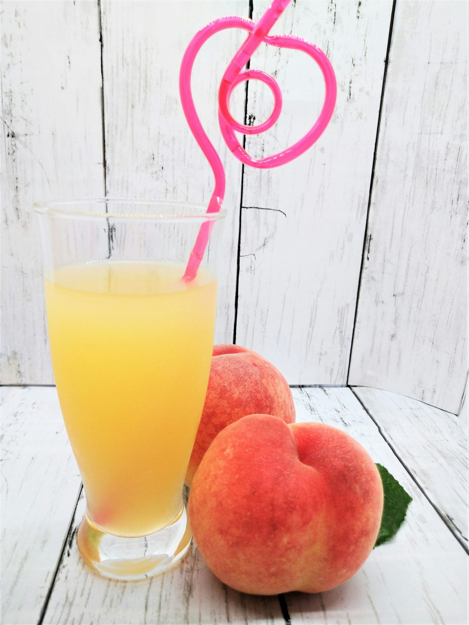 Un bicchiere di succo d'arancia con una cannuccia rosa e due pesche su un tavolo di legno