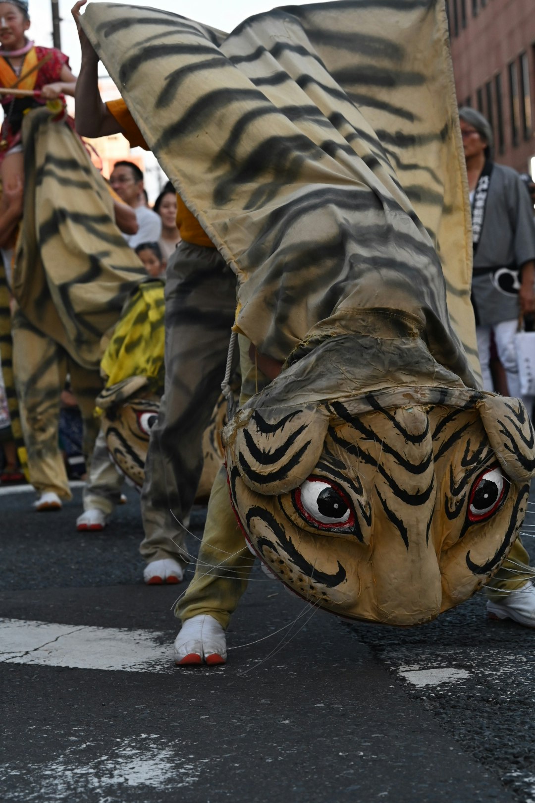 虎の仮面をかぶった踊り手が路上を練り歩く祭りの行列