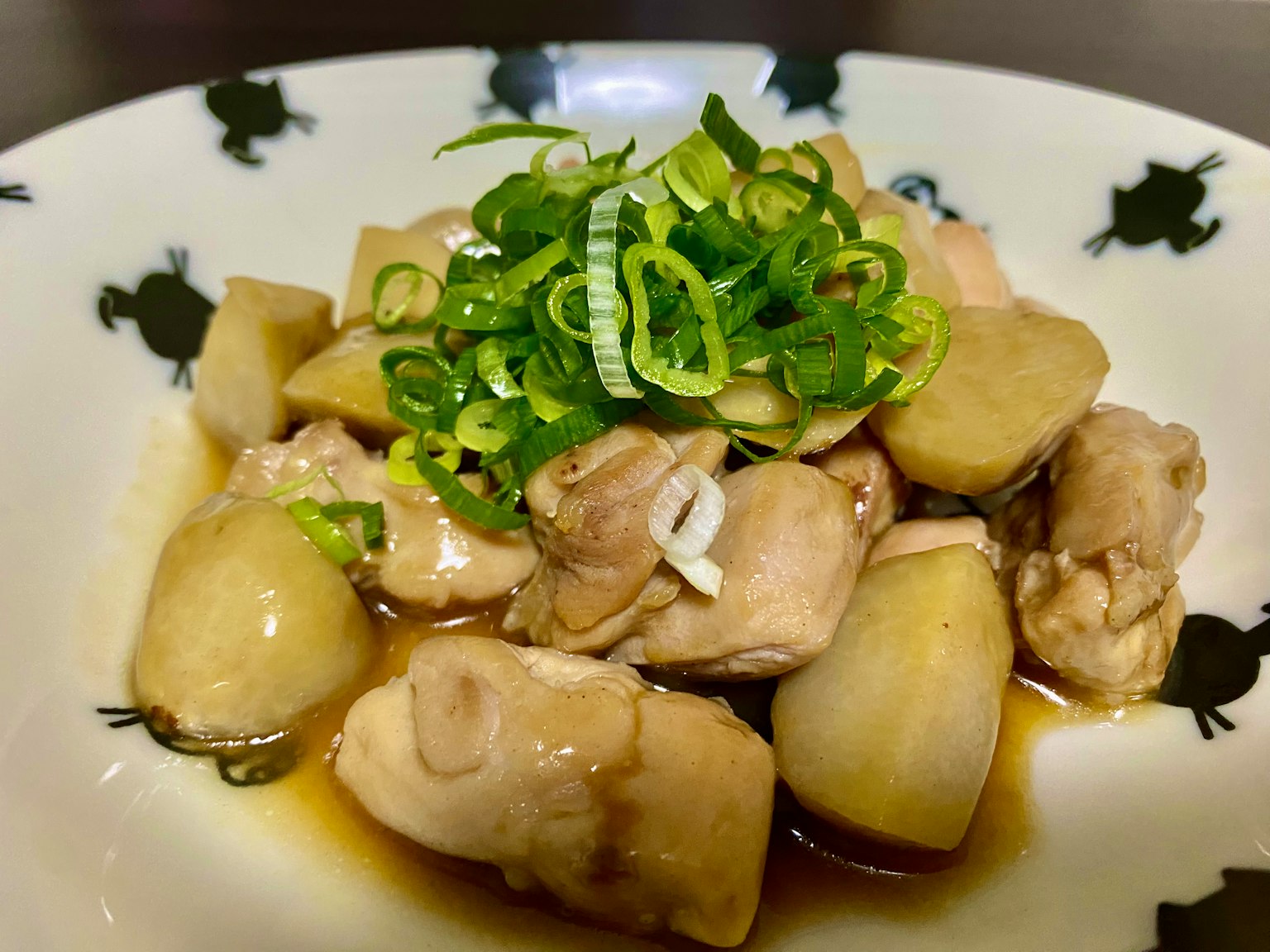 Món gà và hành xanh được phục vụ trên đĩa trắng có thiết kế hình ếch