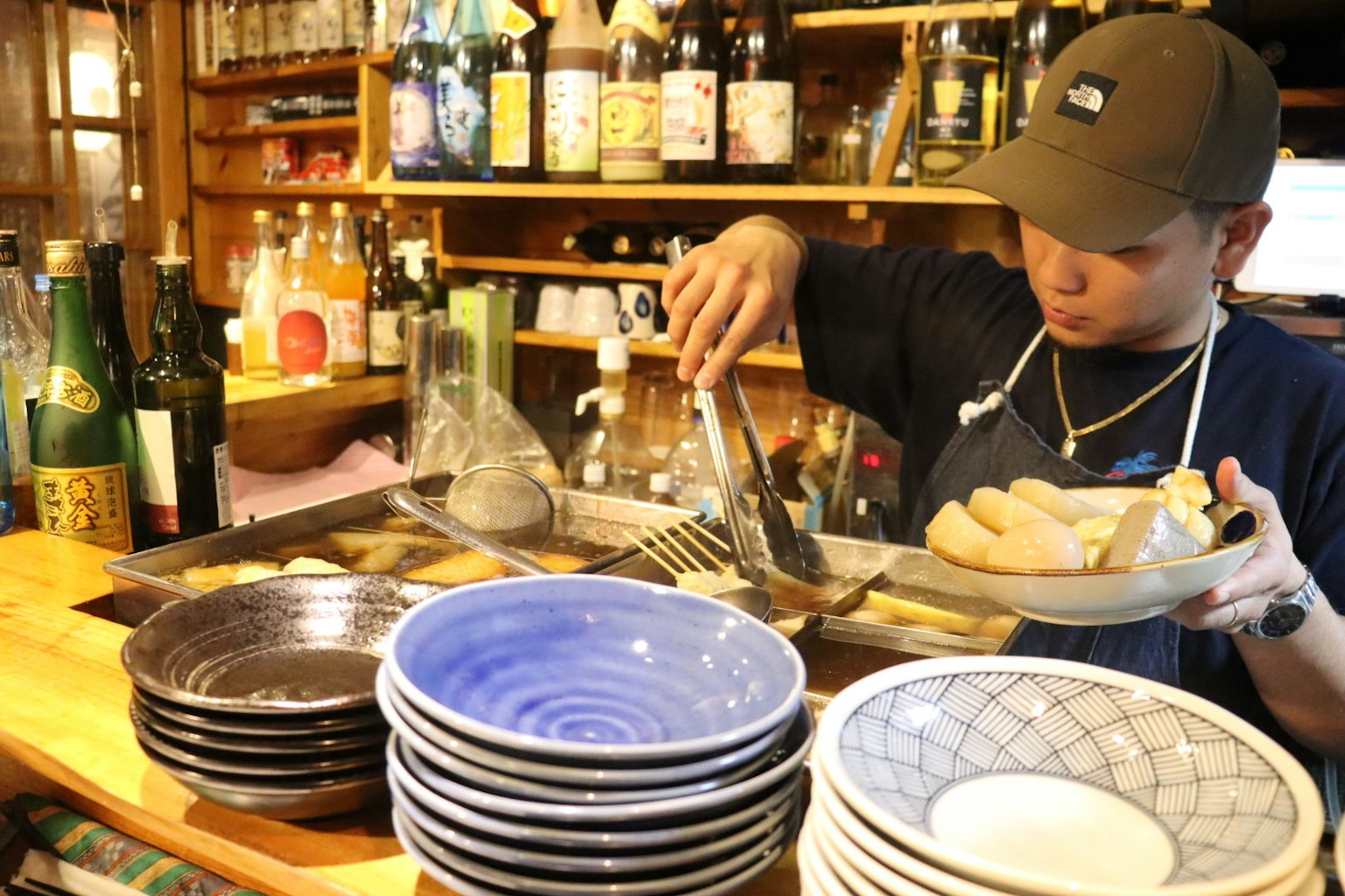 Chef che prepara cibo al bancone con piatti e bottiglie sullo sfondo