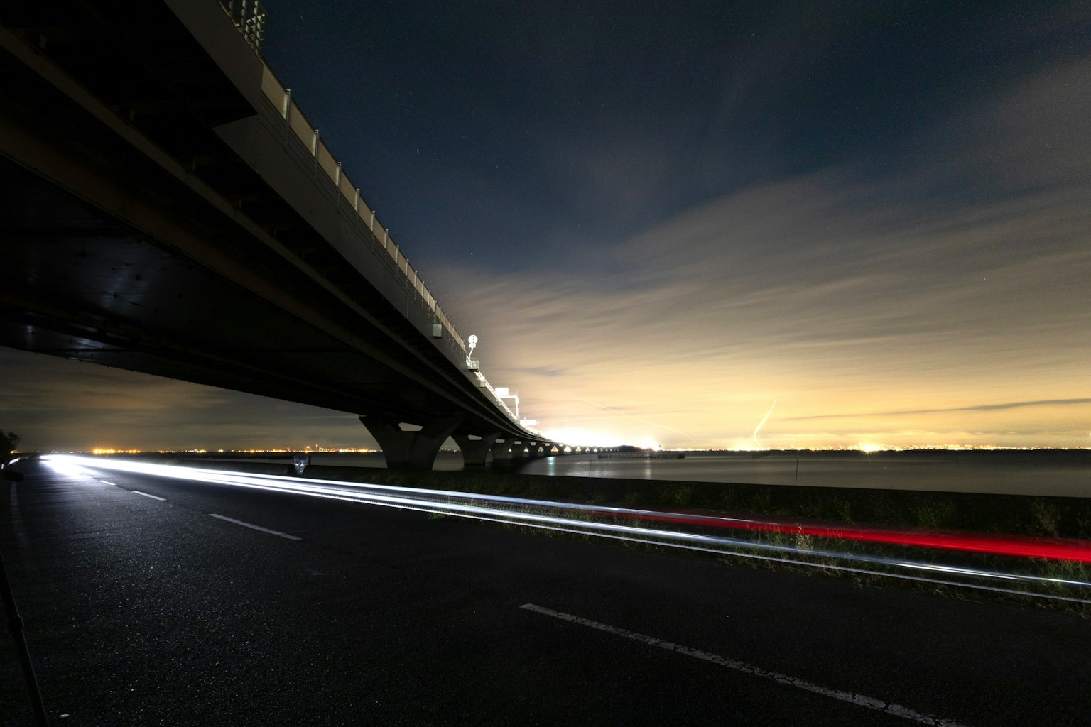 View from under a bridge at night with flowing car lights and colorful sky