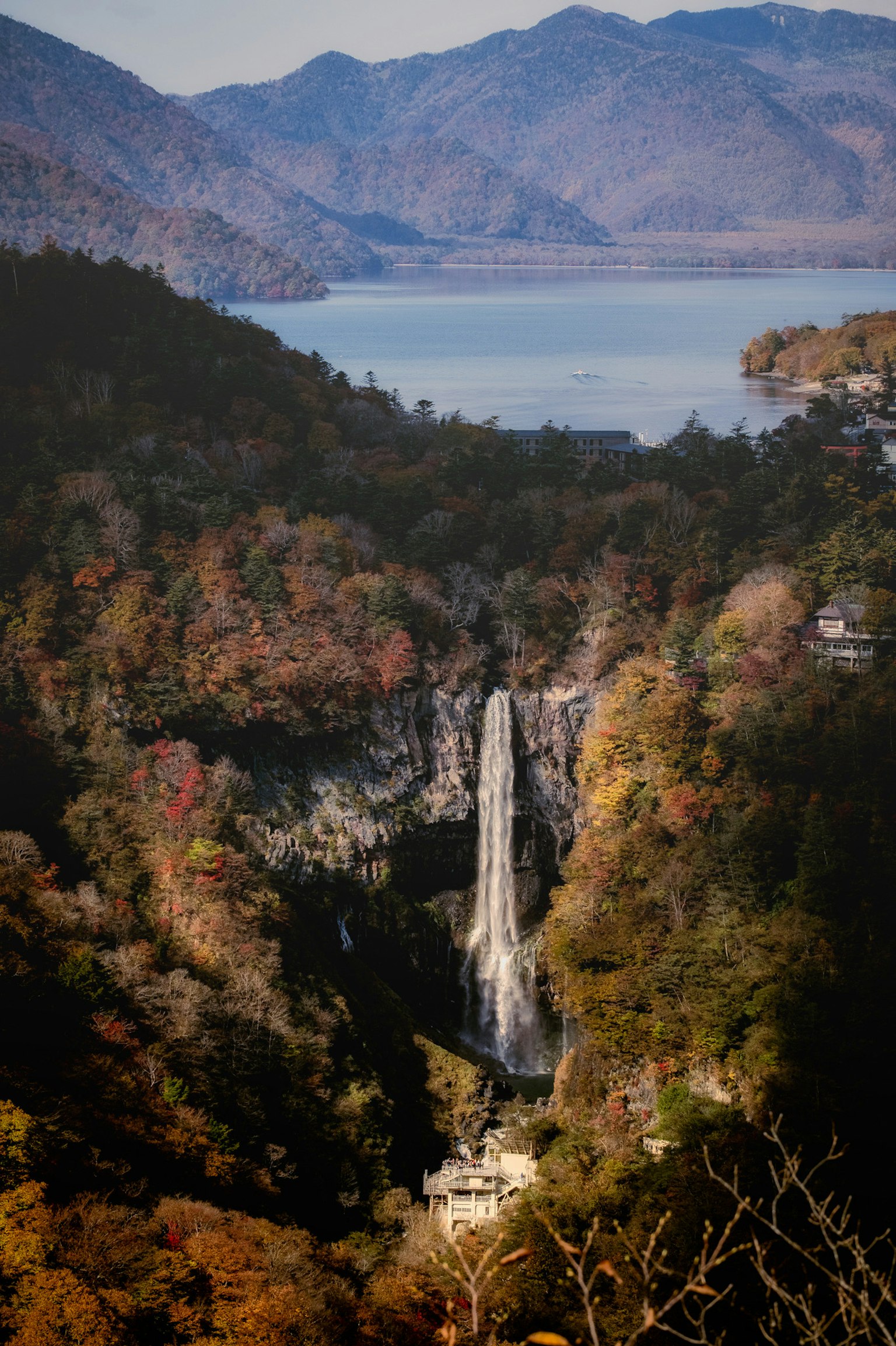 Vista escénica de una cascada rodeada de follaje otoñal con montañas y un lago al fondo