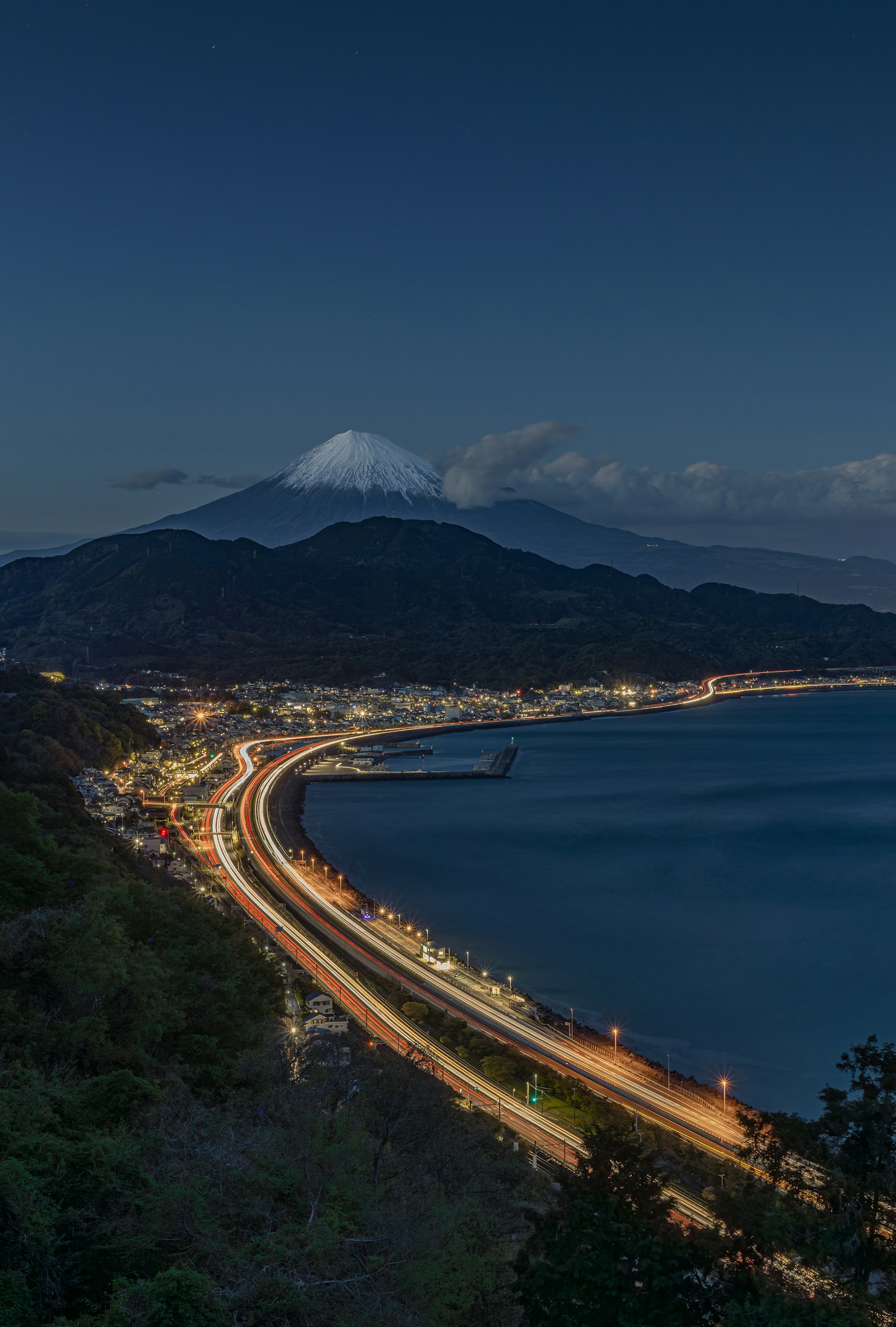 富士山を背景にした夜の海岸線の風景 車のライトが道路を照らす