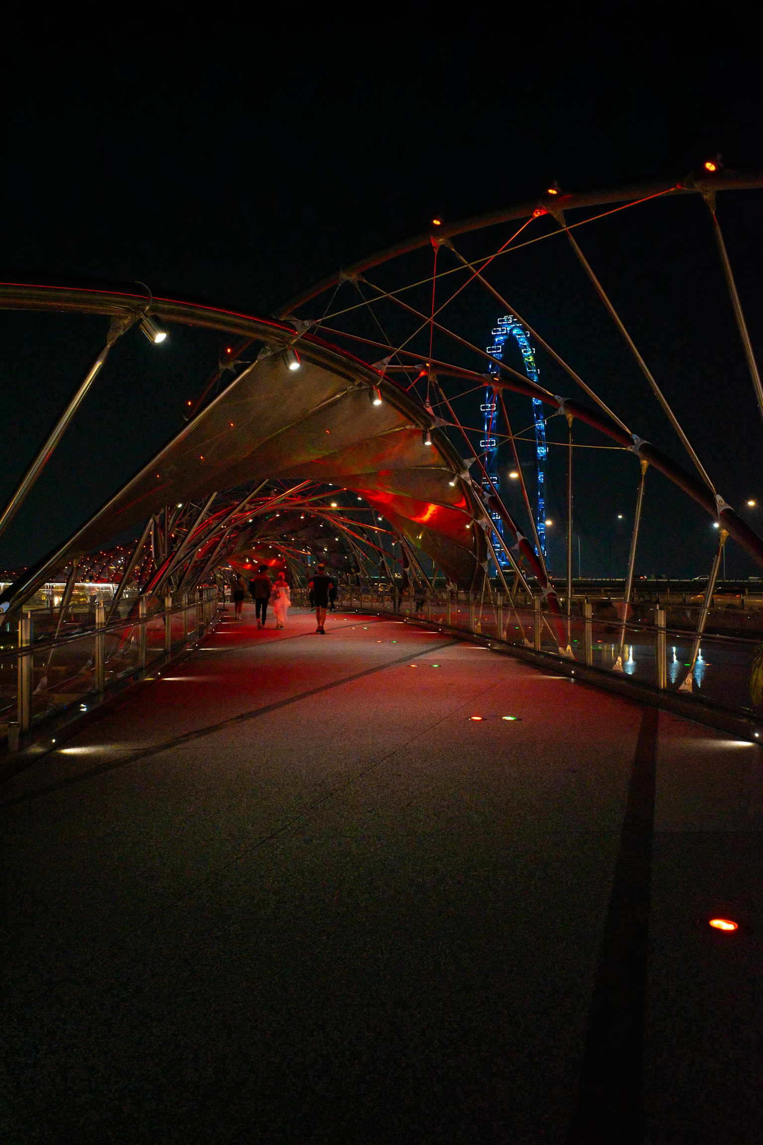 Night view of a bridge with red lighting and a ferris wheel in the background
