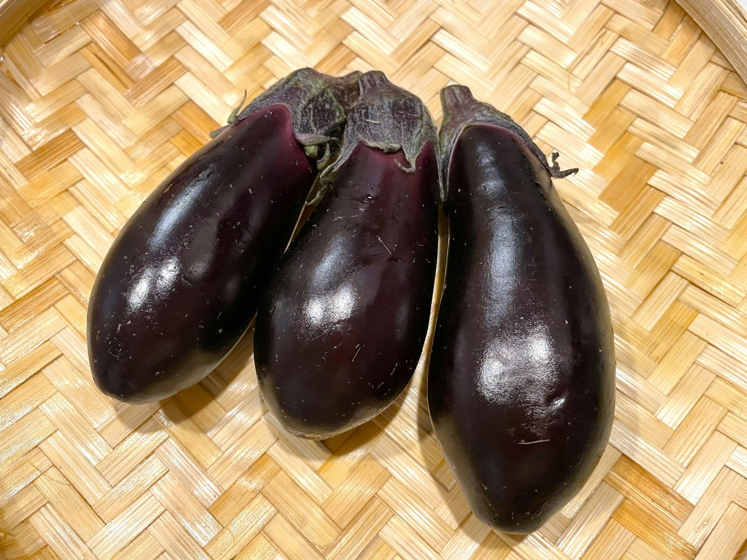 Tiga terong dengan kulit ungu mengkilap dalam keranjang anyaman