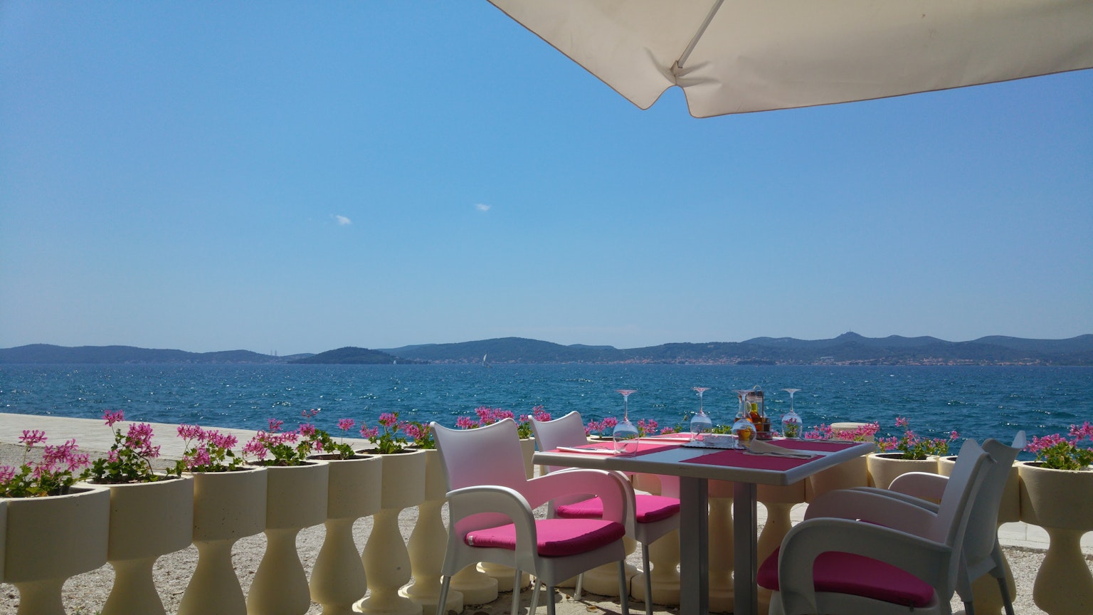 Terrace table with pink chairs overlooking blue sea and mountains