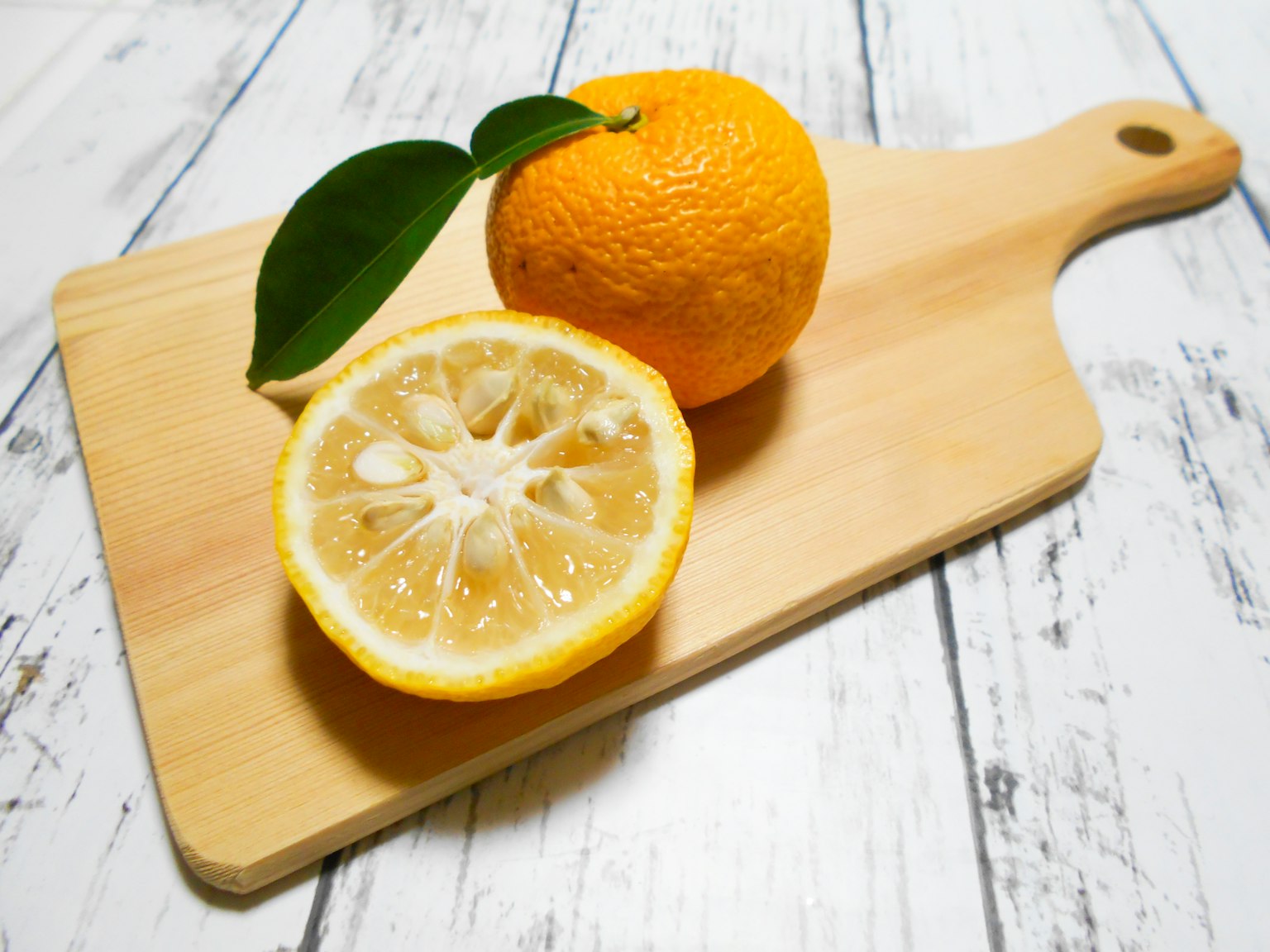 Photo of an orange and a halved lemon on a wooden cutting board