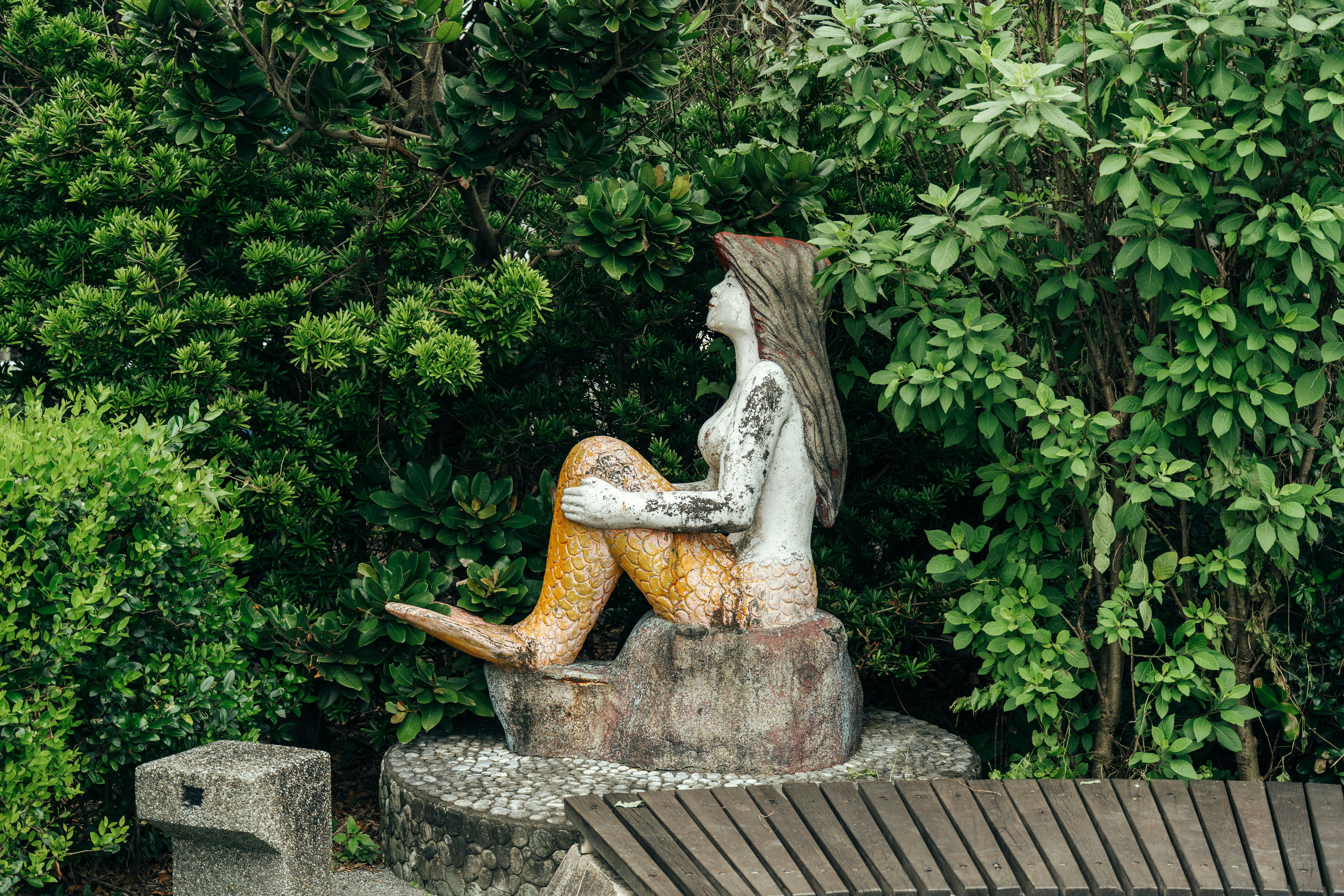 statua di sirena in pietra e panchina davanti a siepi verdi