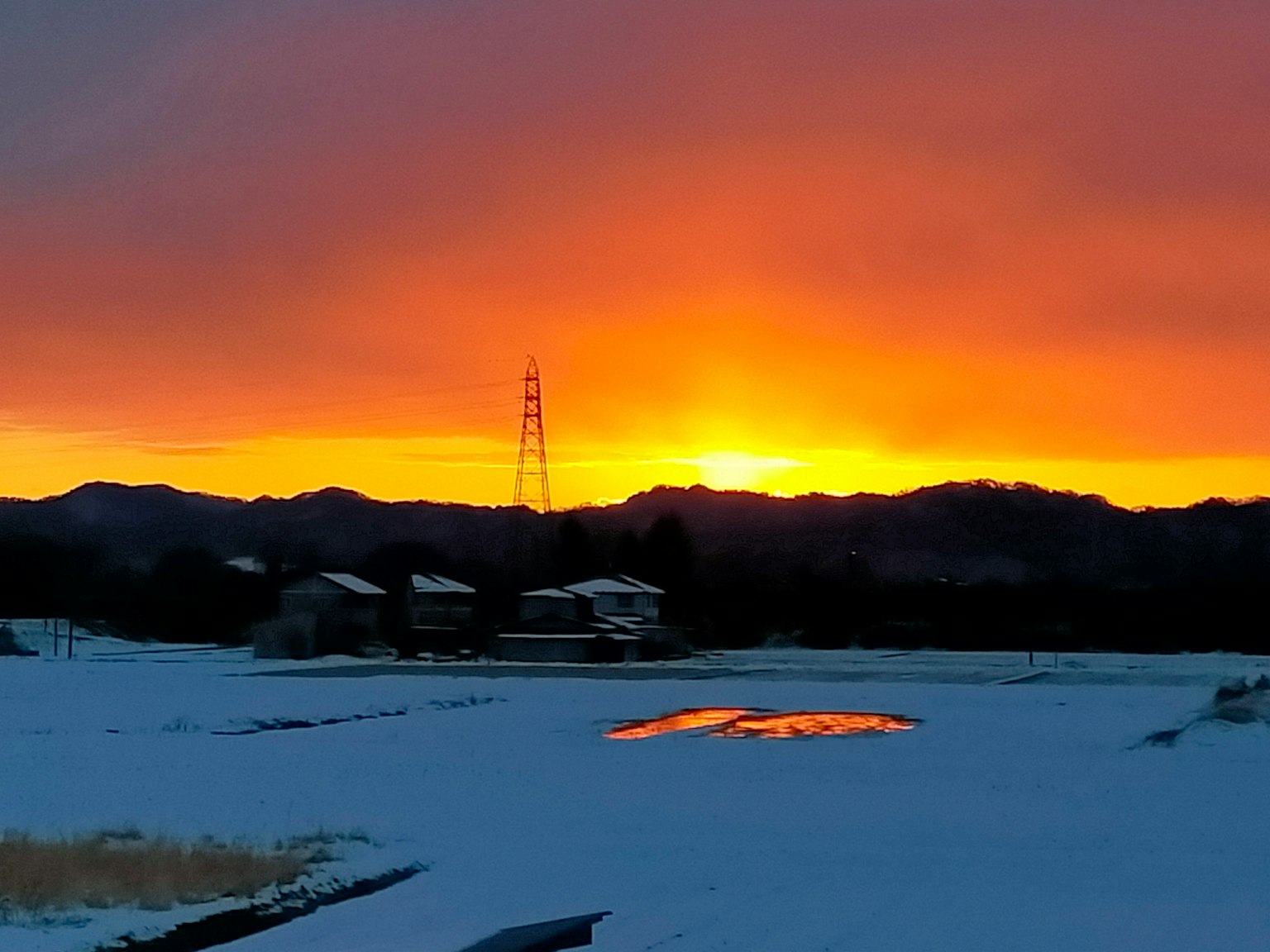 Mit Schnee bedeckte Felder mit einem Sonnenuntergang, der sich in den Bergen spiegelt