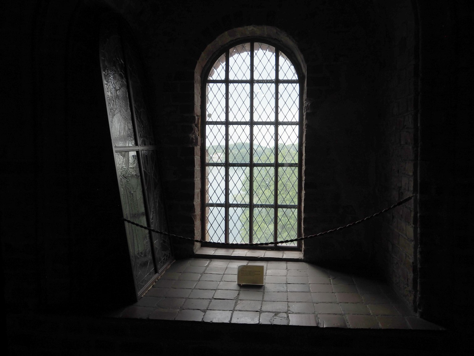 Una stanza poco illuminata con una finestra che lascia entrare la luce all'esterno si vede un paesaggio verde