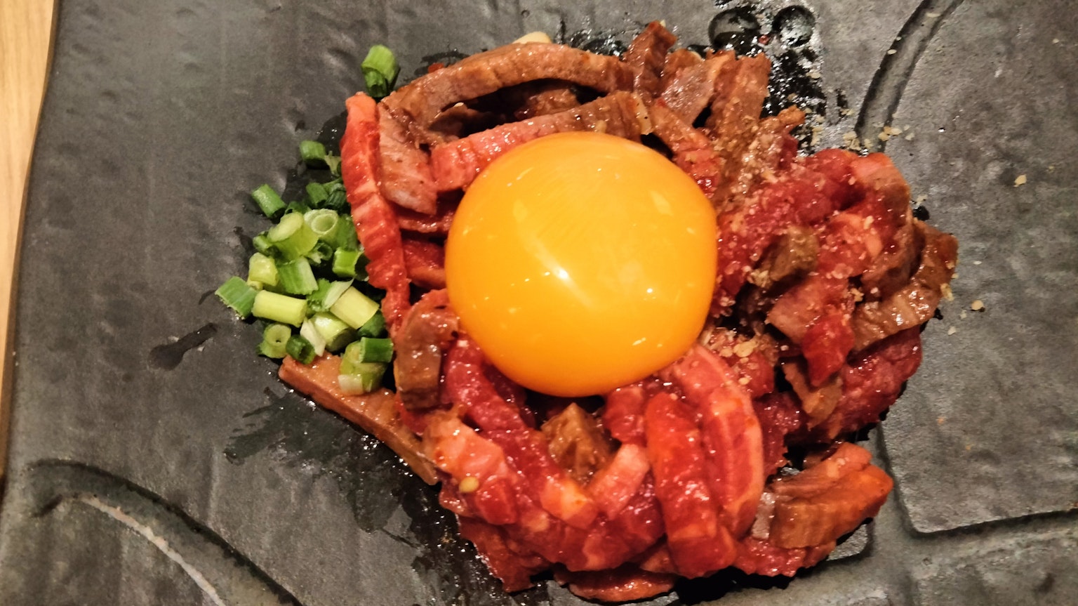 검은 접시에 생 계란과 조리된 고기가 배열된 요리