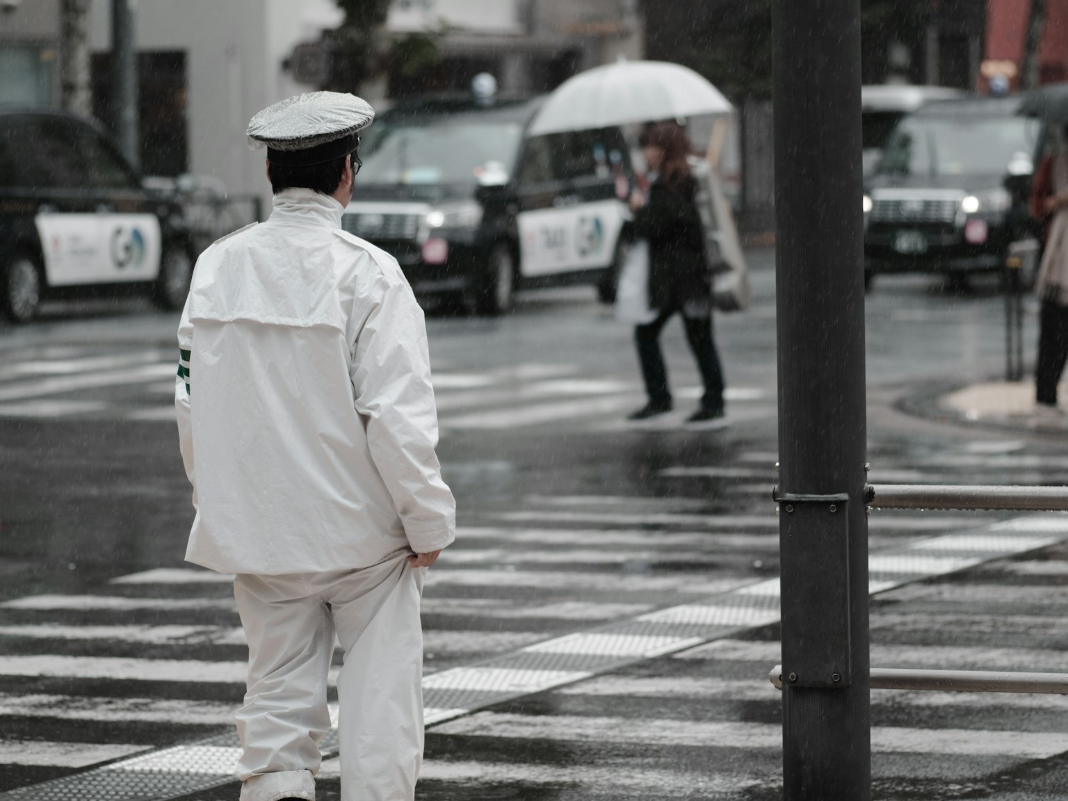 ตำรวจจราจรในชุดขาวเฝ้าสังเกตทางข้ามในวันที่ฝนตก