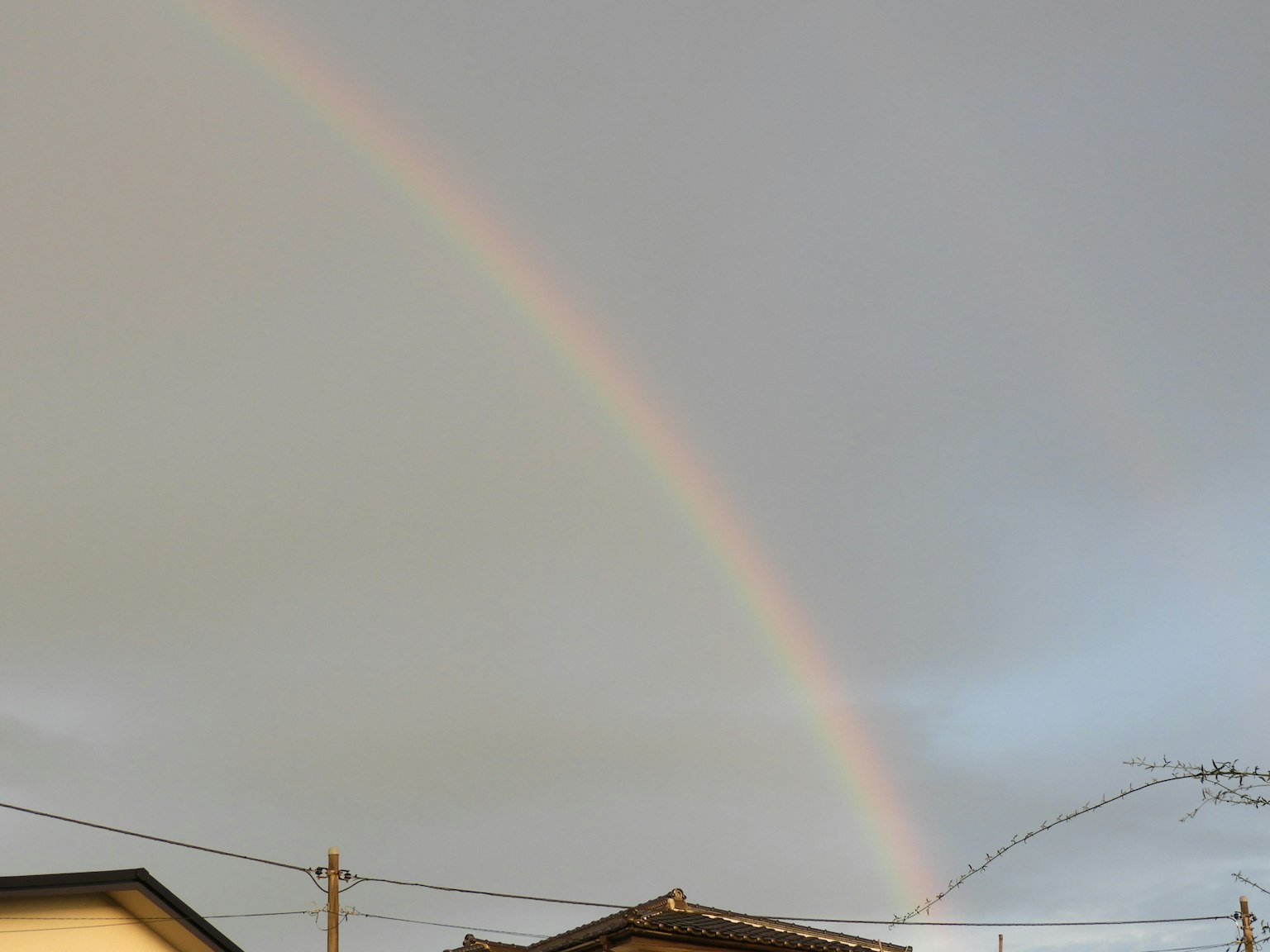 Un arc-en-ciel se dressant au-dessus d'un ciel nuageux avec des toits au premier plan