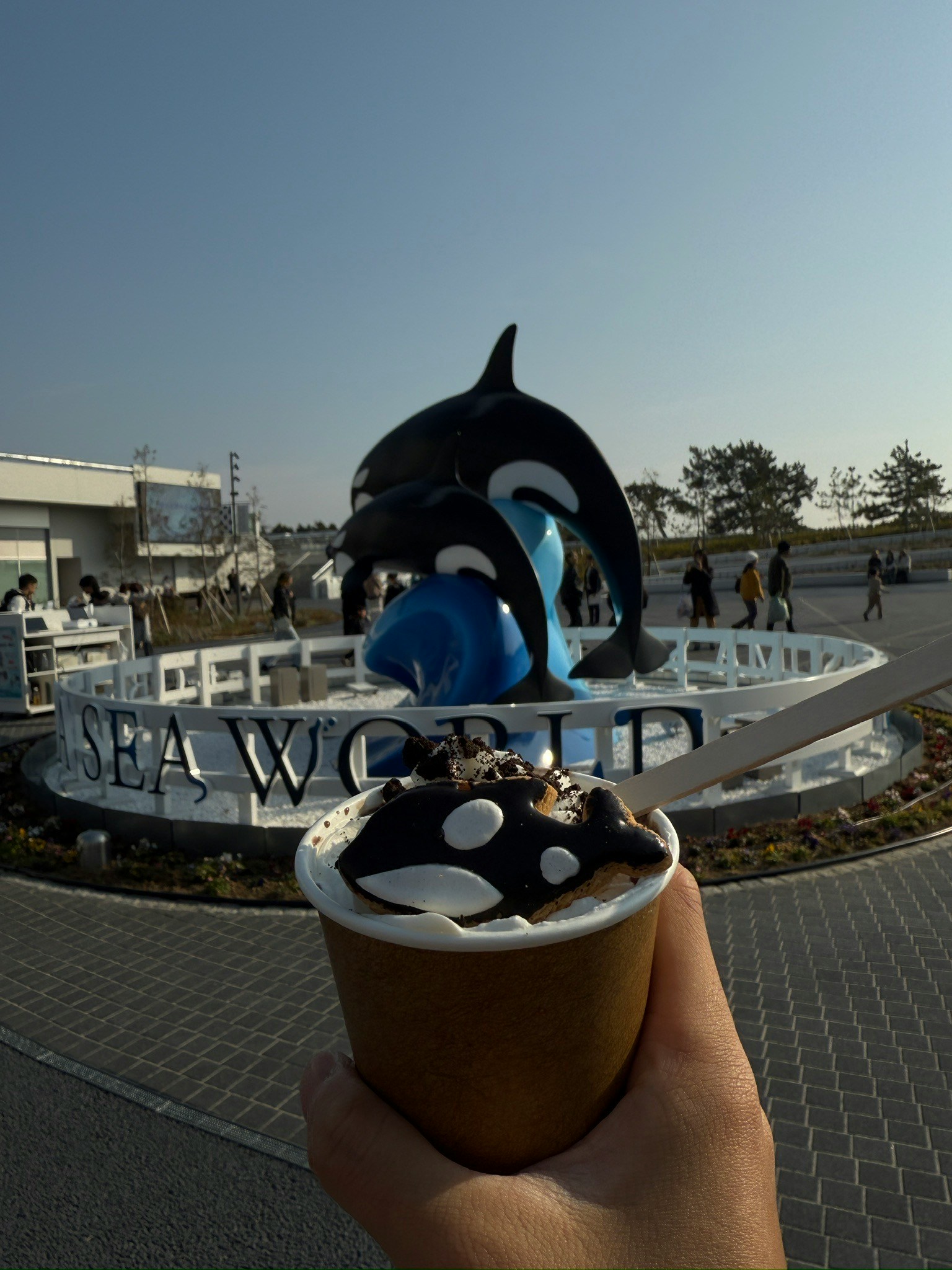 A hand holding ice cream in front of a SeaWorld sign and orca statue