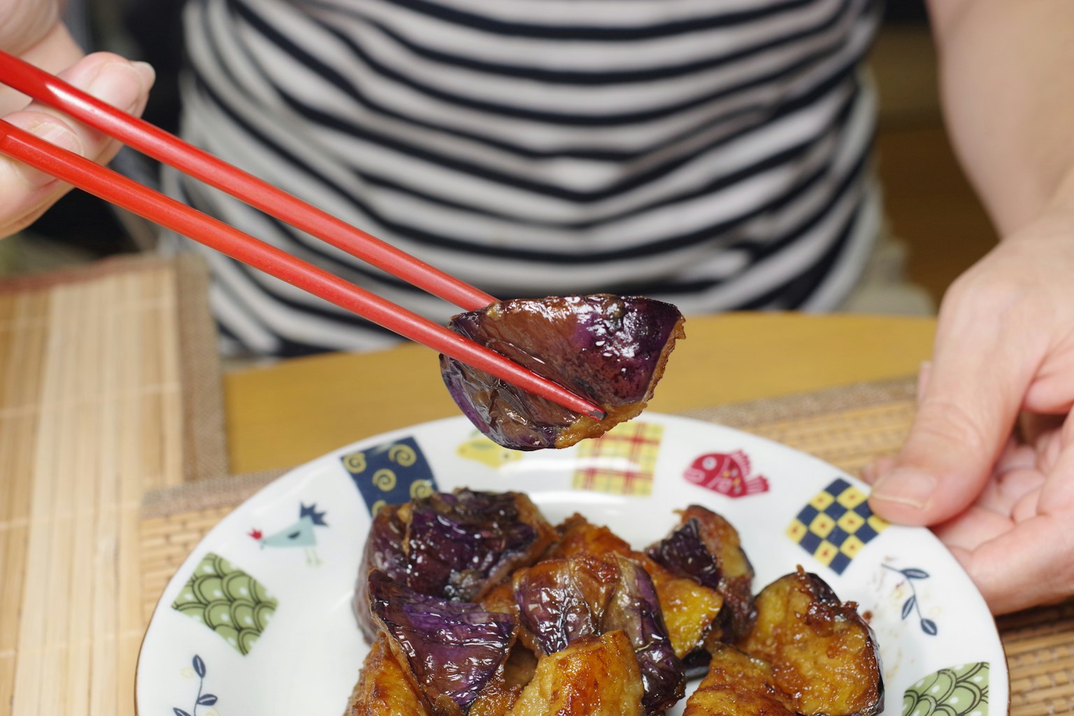 Une main tenant des baguettes prenant de l'aubergine grillée