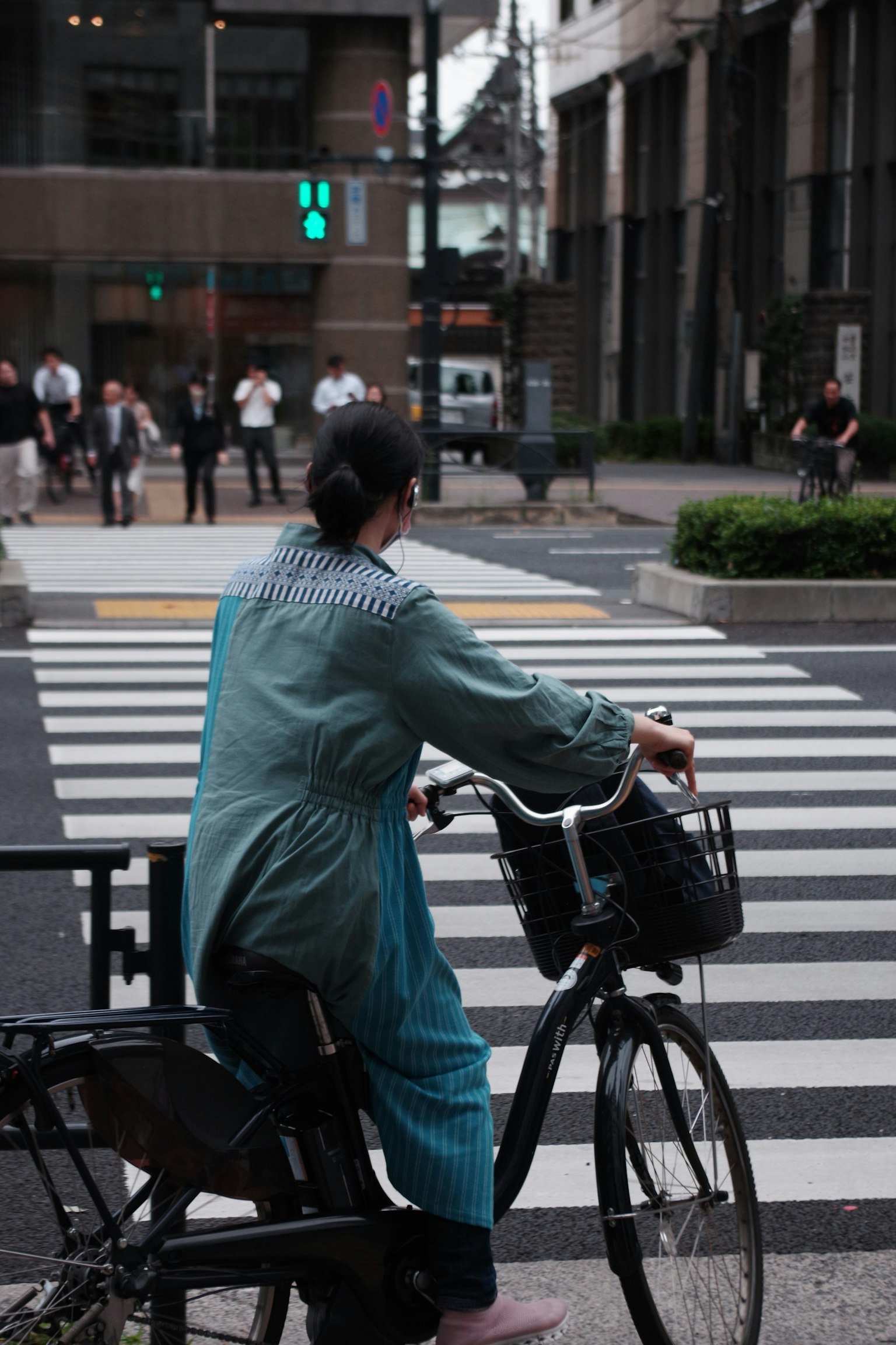Wanita berpakaian biru menunggu di sepeda di zebra cross