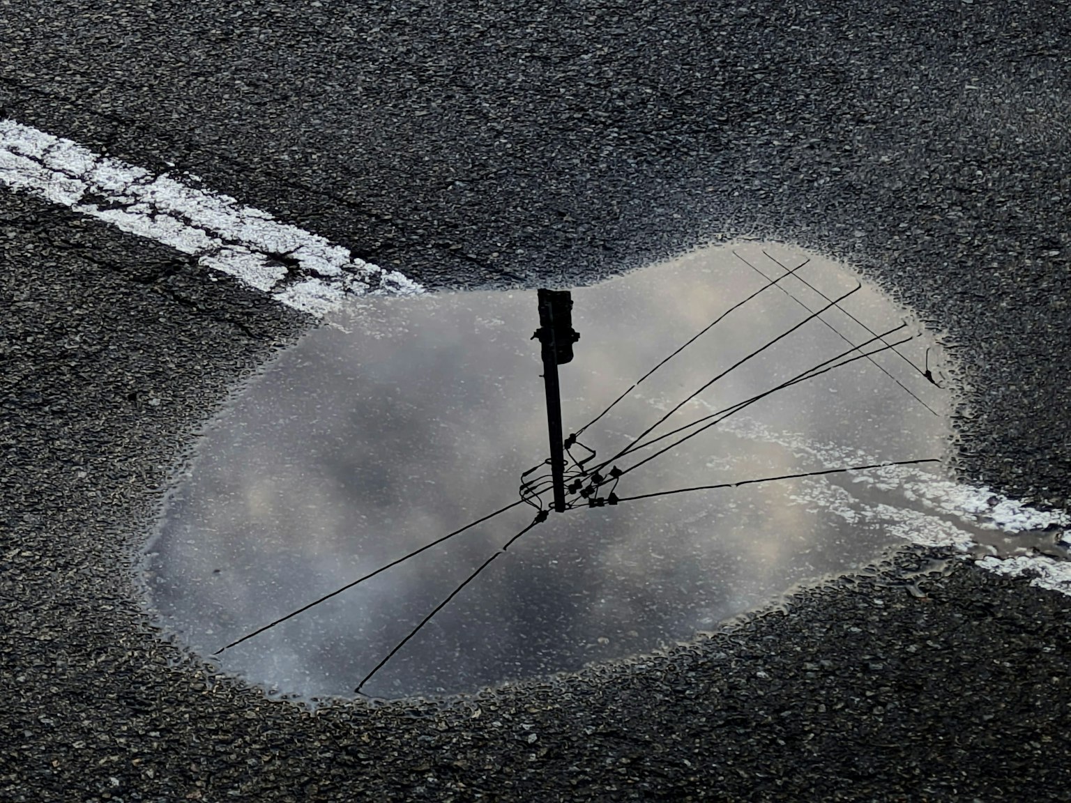 Puddle on the road reflecting the sky and a utility pole