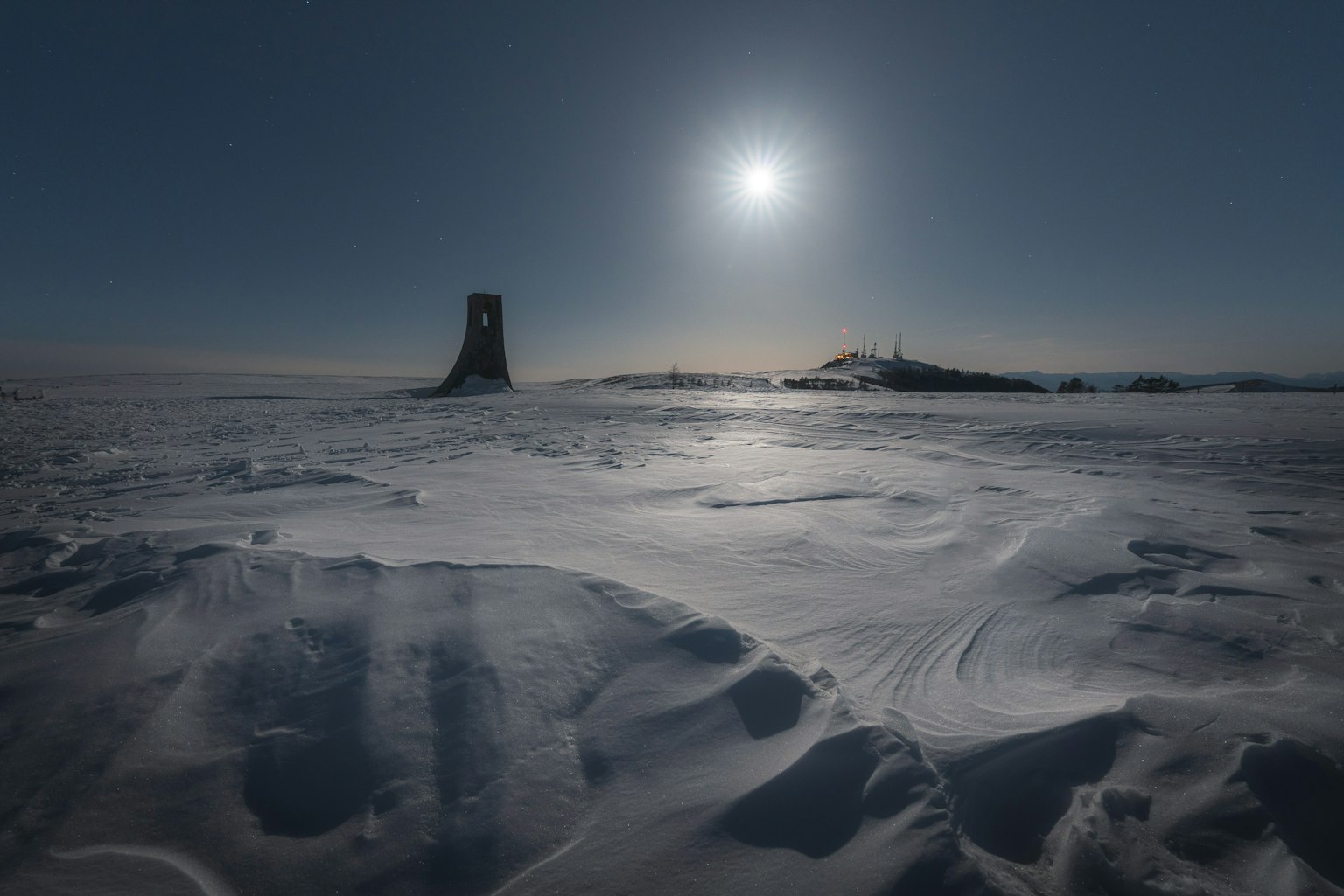 Snow-covered landscape with a distant tower and sun