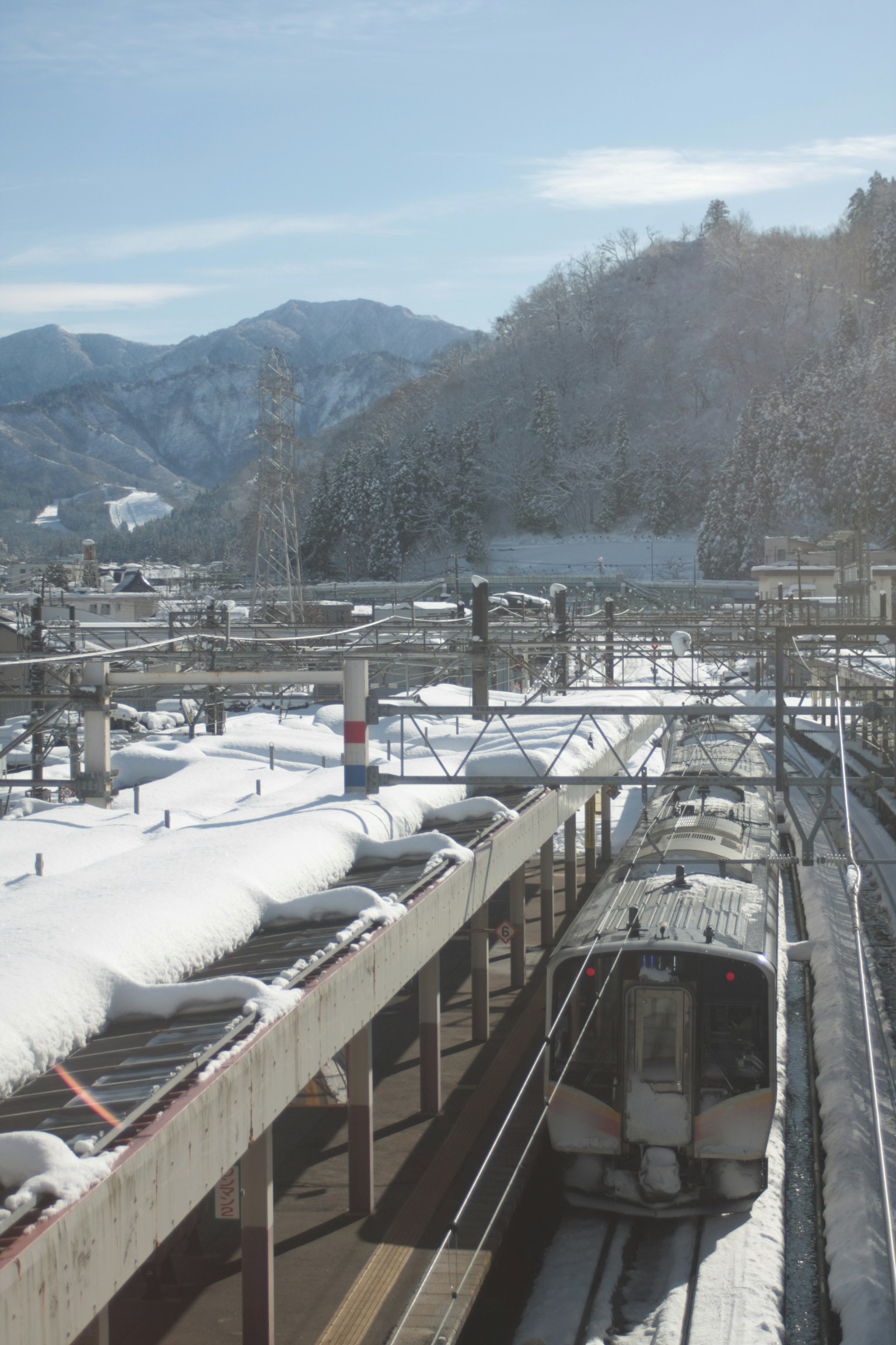 สถานีรถไฟที่ปกคลุมไปด้วยหิมะและภูเขาในพื้นหลัง