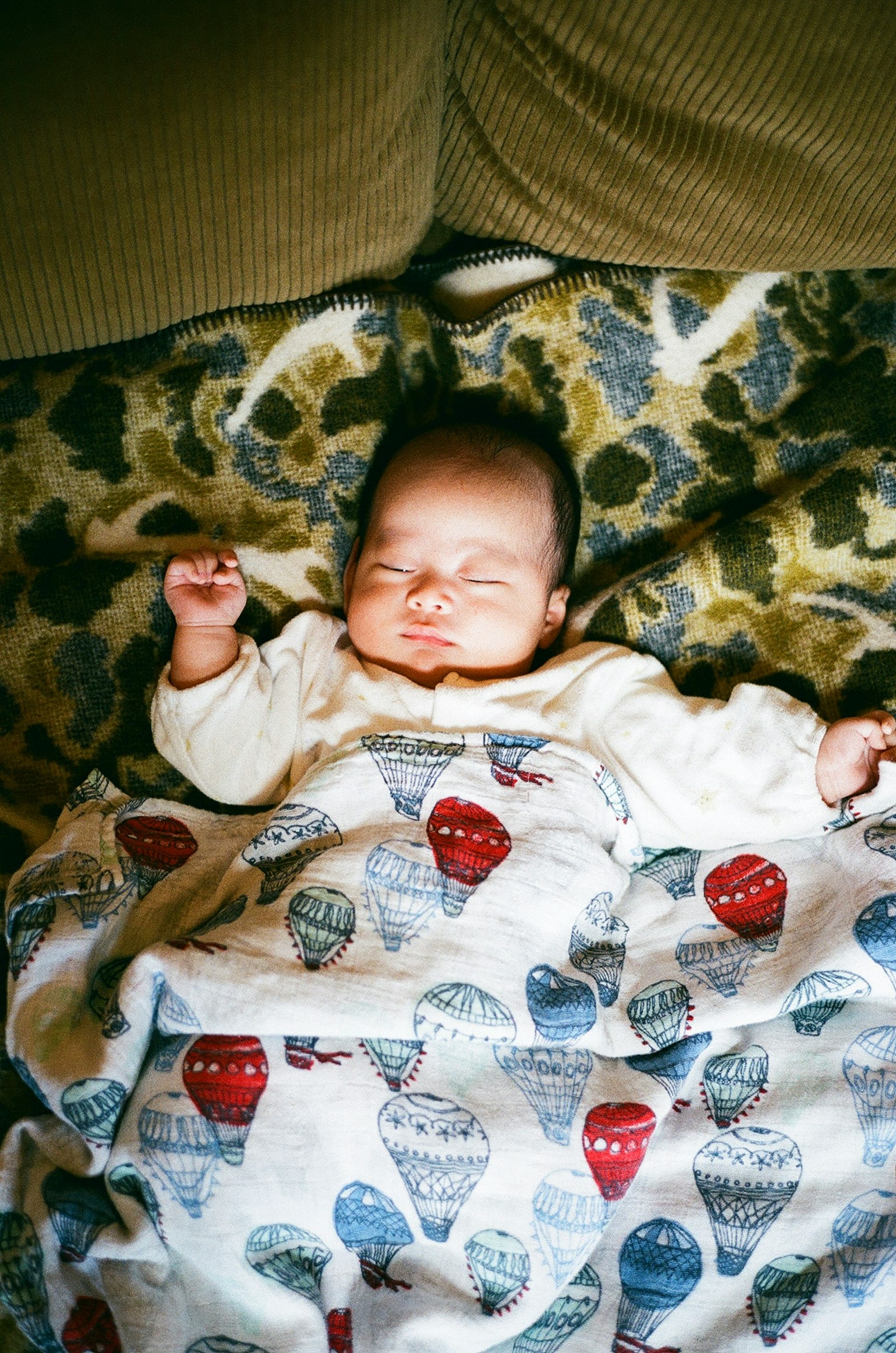 Un bambino che dorme pacificamente avvolto in una coperta con motivi di mongolfiere