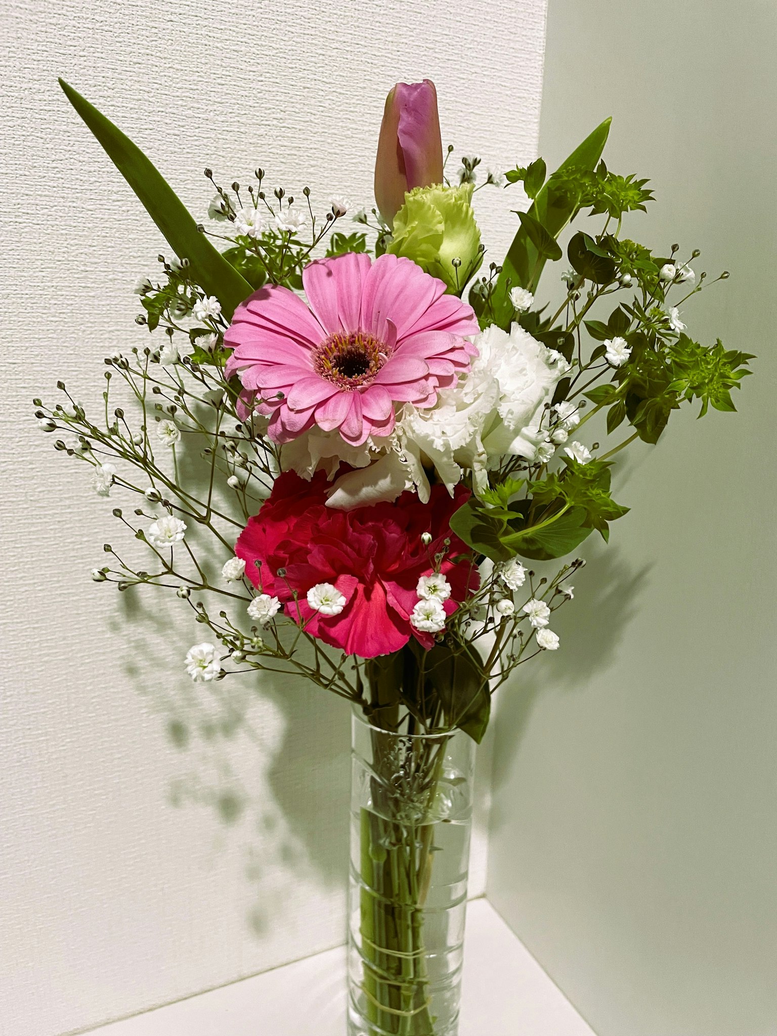 Un bouquet con gerbera rosa e garofano rosso in un vaso trasparente