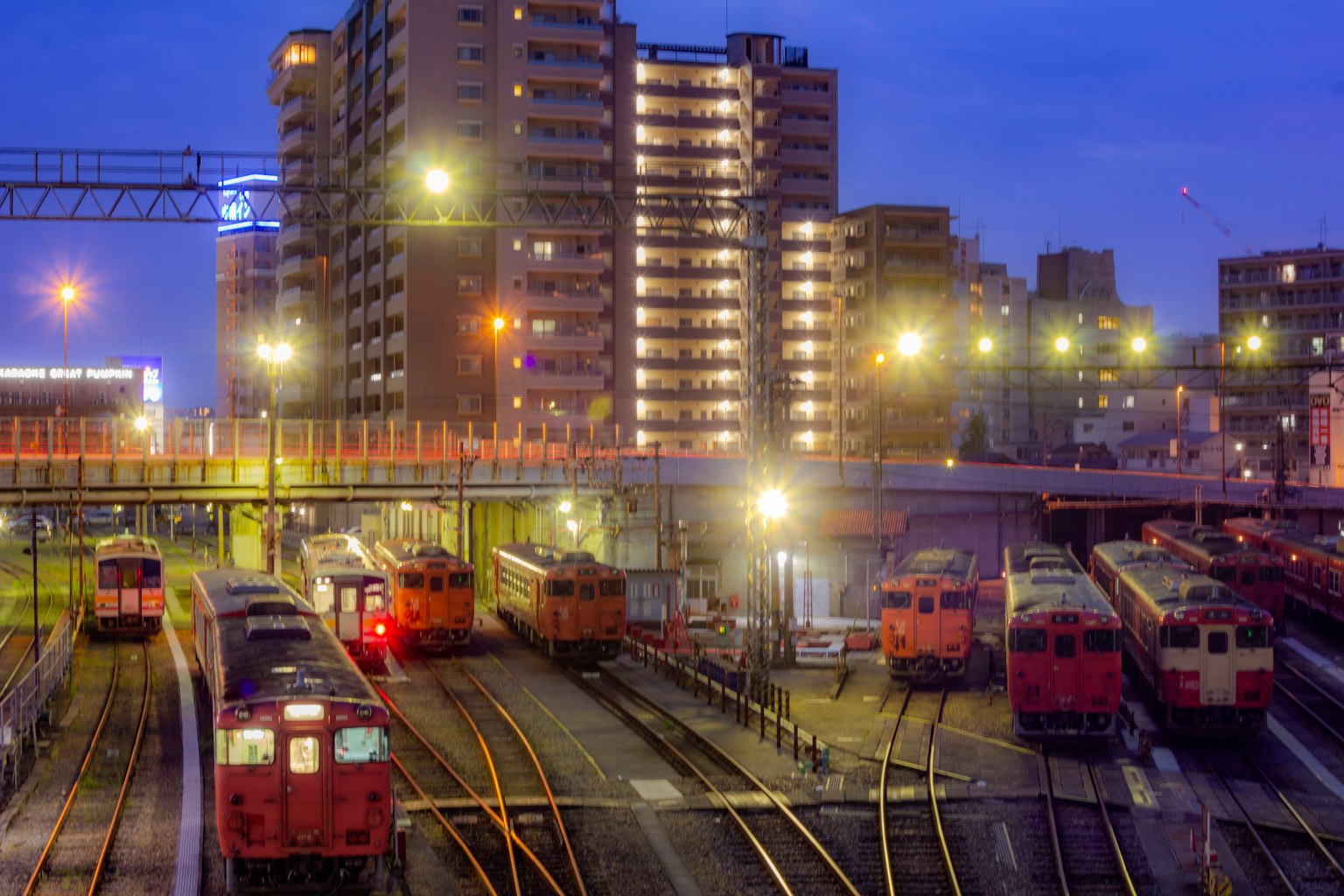 Scena di stazione ferroviaria notturna con più treni e grattacieli