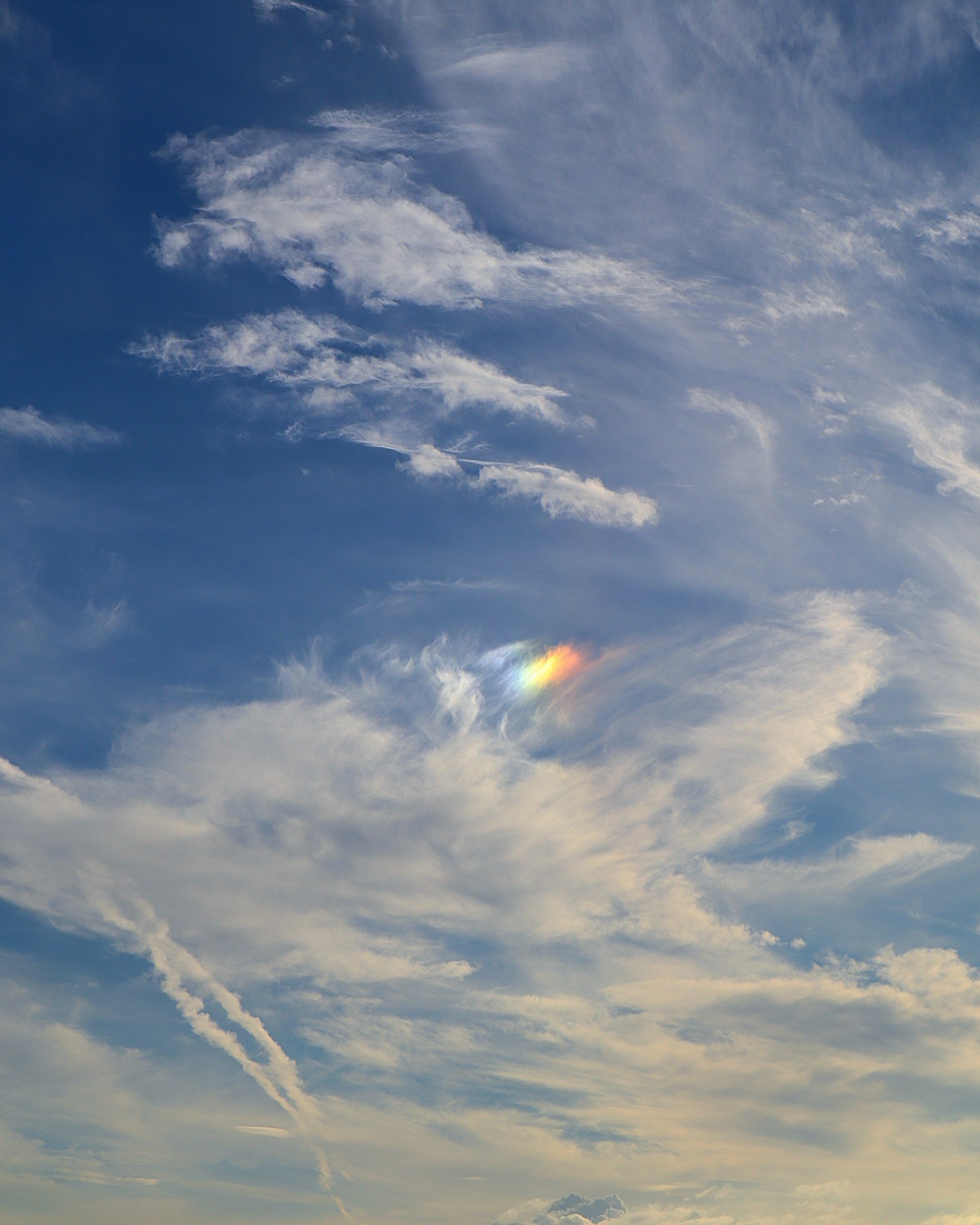 Ein kleiner Regenbogen erscheint zwischen den Wolken in einem blauen Himmel