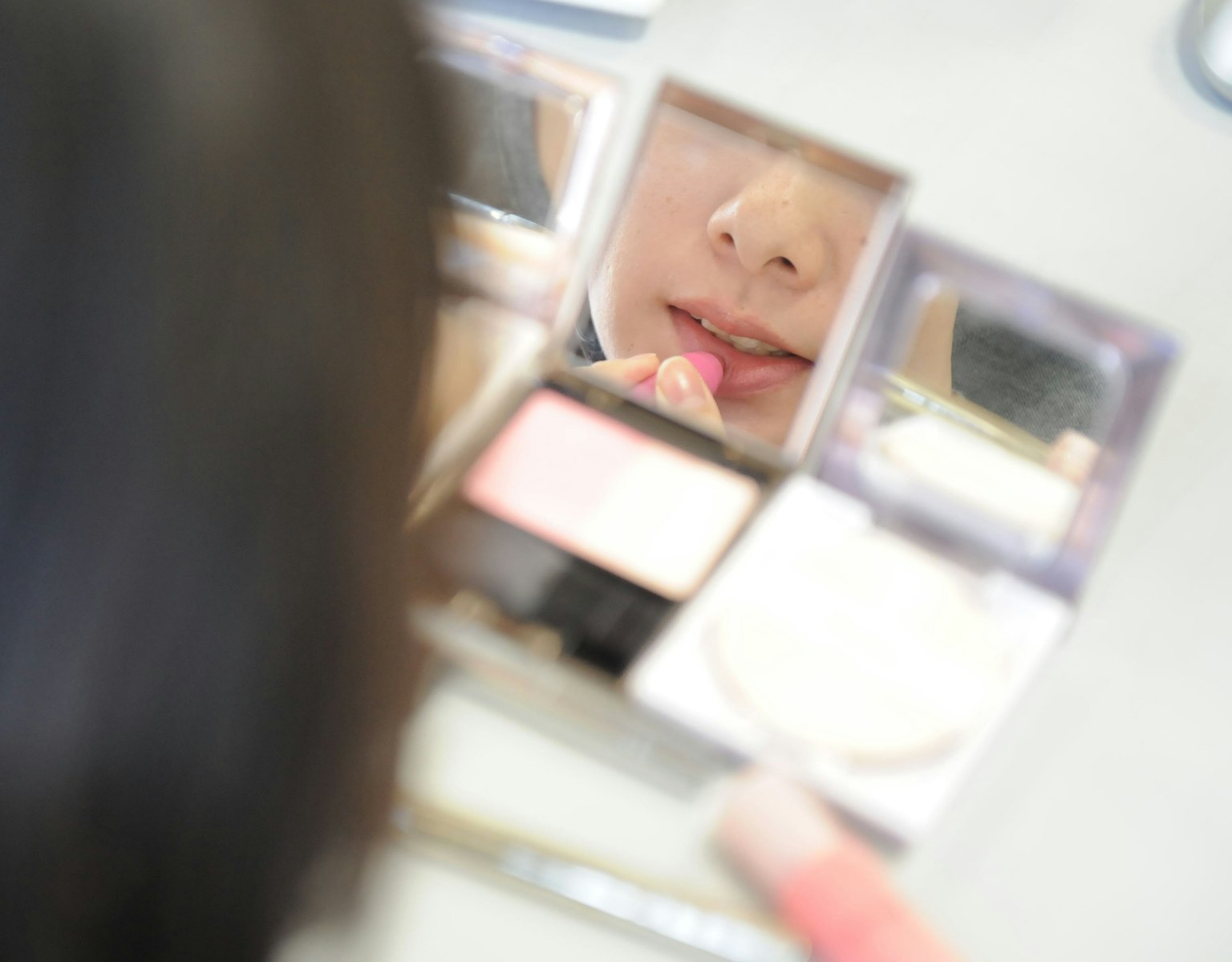 Nahaufnahme einer Person, die Lippenstift aufträgt und in einen Spiegel schaut