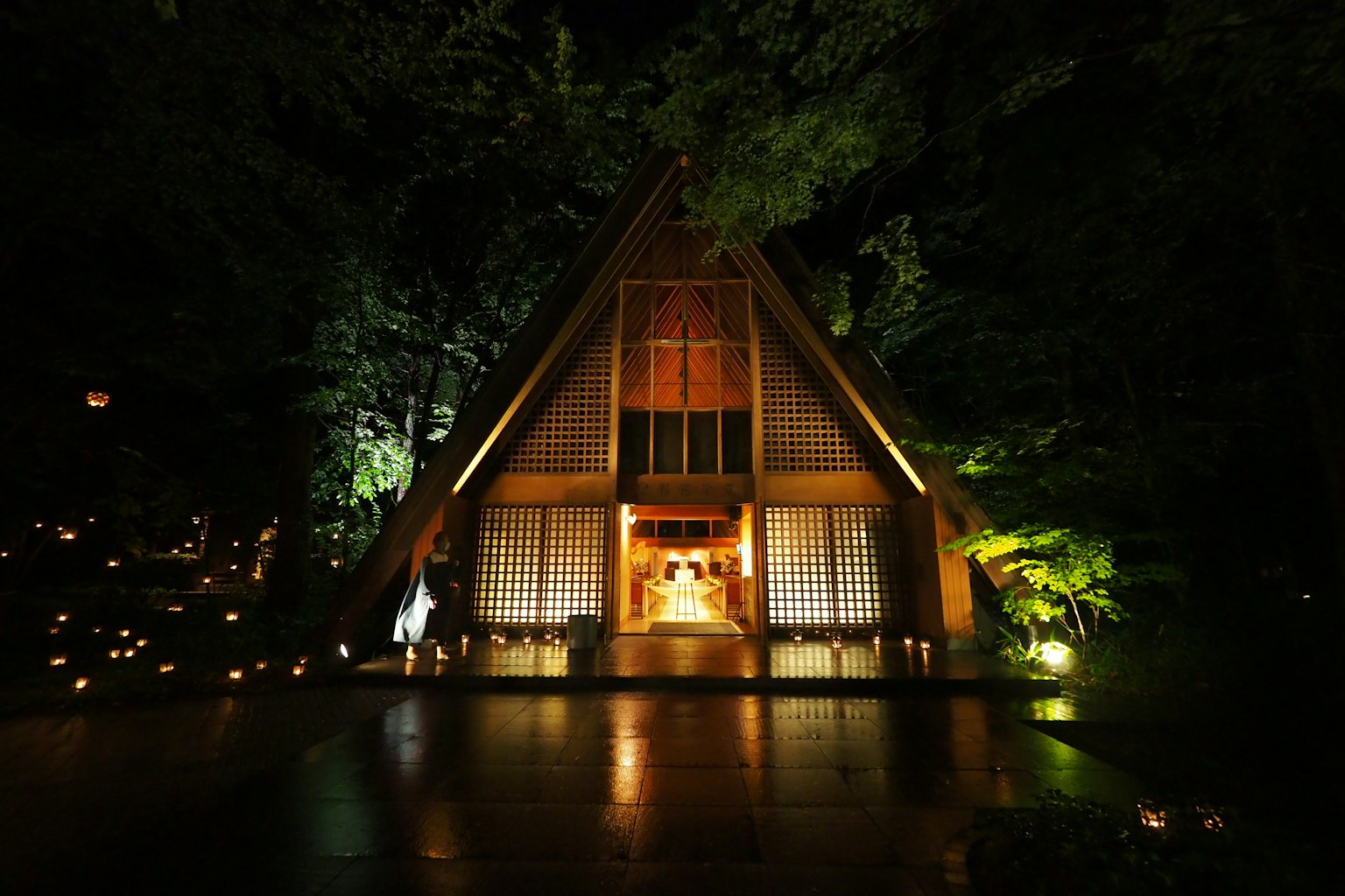 Un hermoso edificio de techo triangular que se encuentra en un bosque nocturno iluminado por luces cálidas
