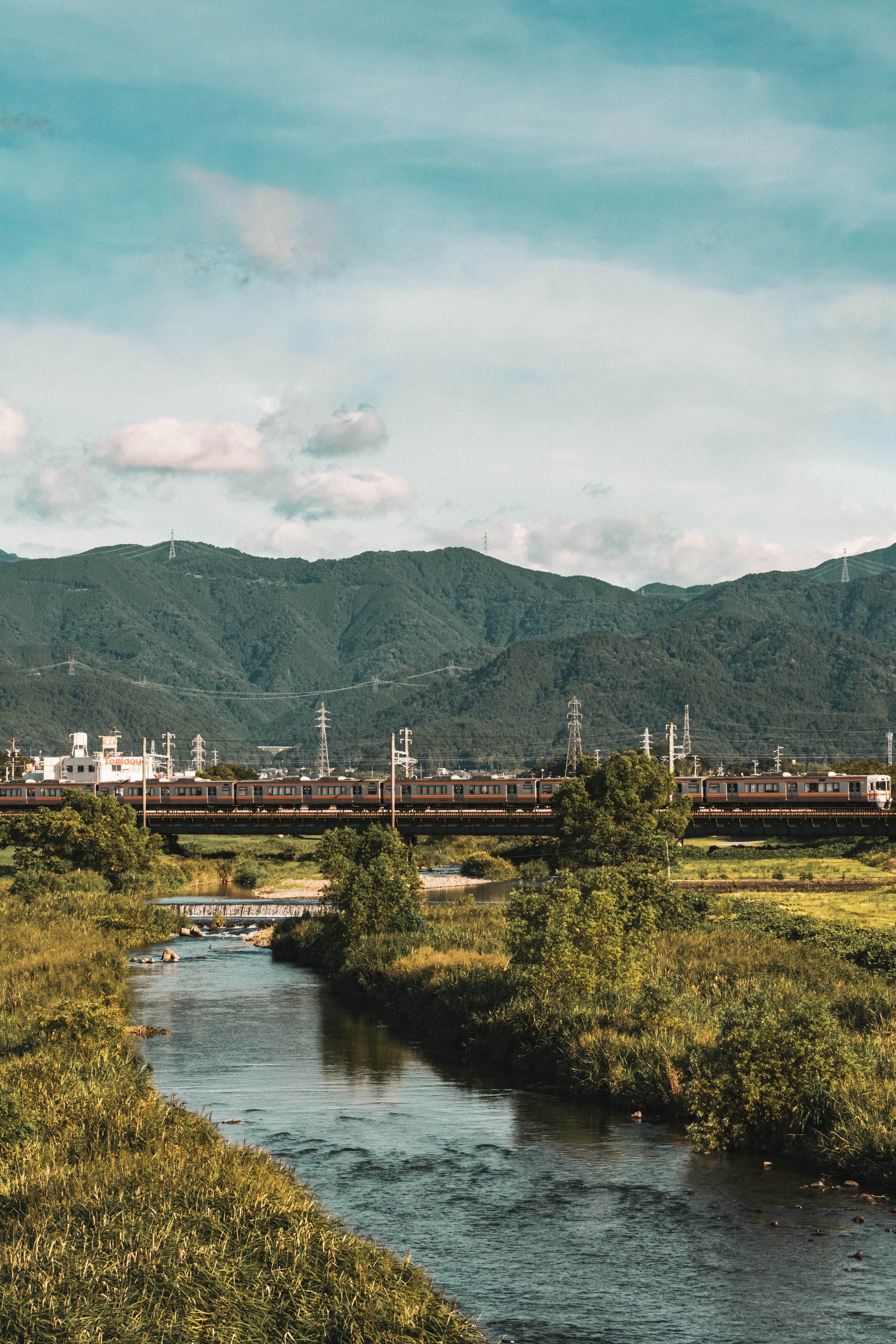 河岸工業景觀，遠處山稜與輸電鐵塔
