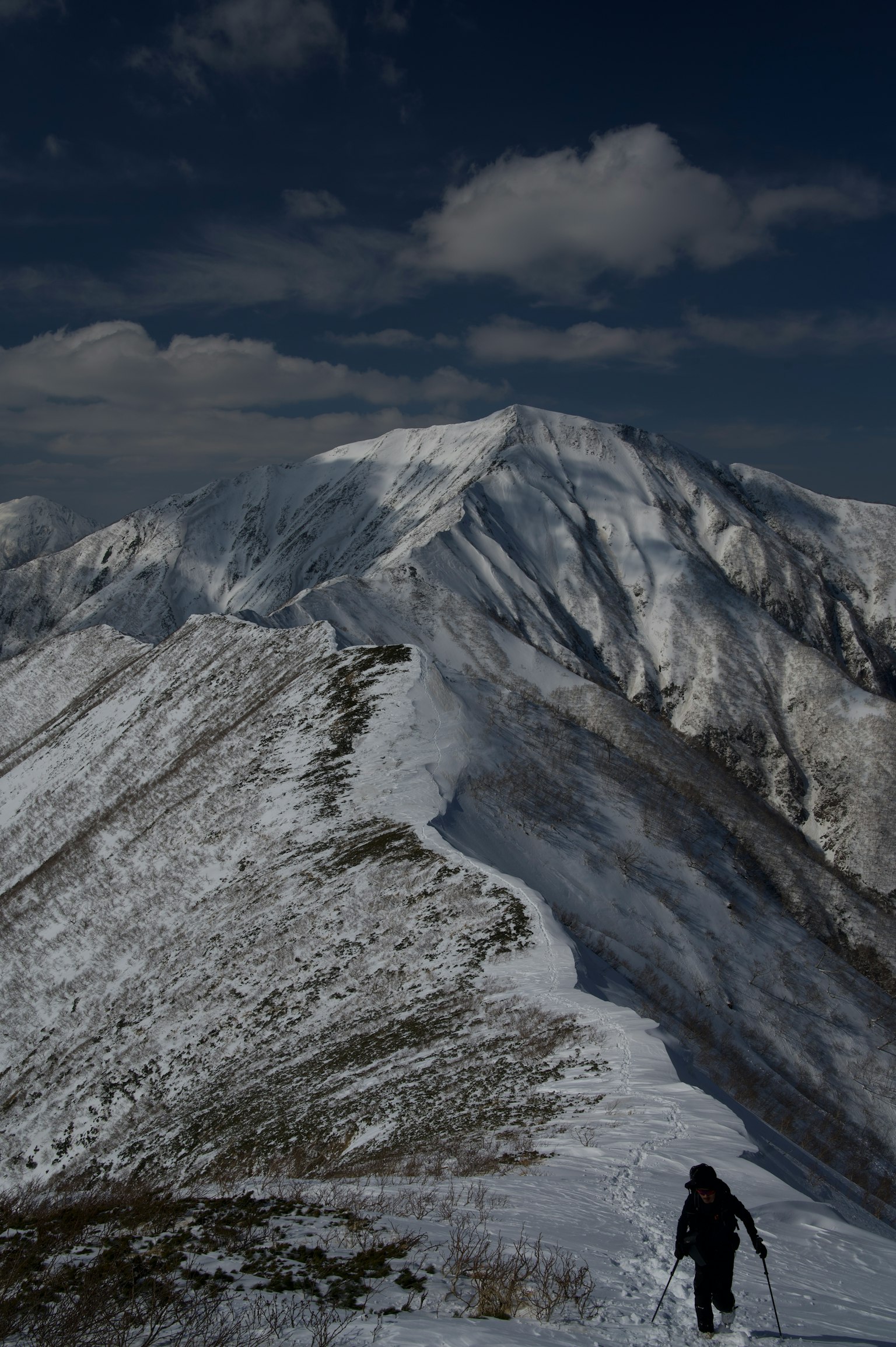 在雪山脊上行走的登山者，背景有戲劇性的山峰