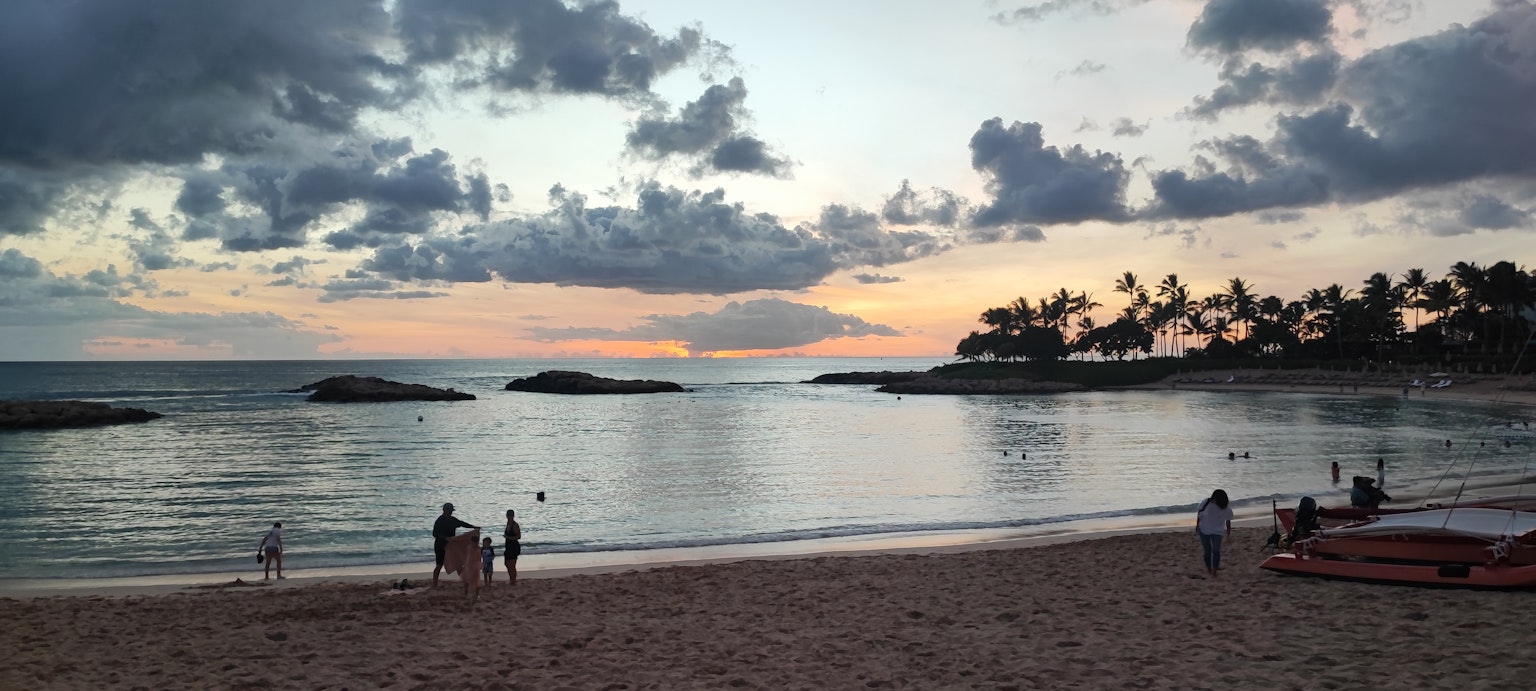 美麗的海灘日落景色人們在海中玩耍平靜的波浪和多雲的天空
