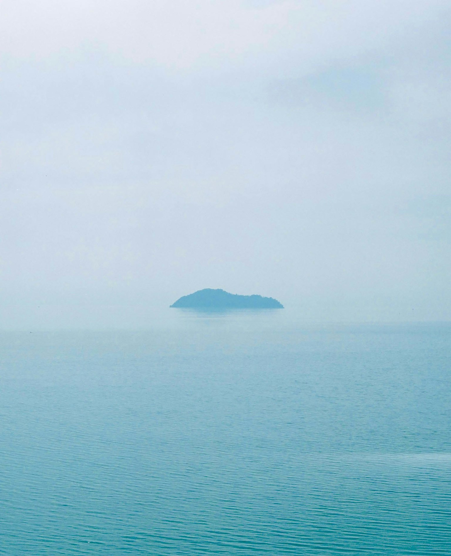 被雾气笼罩的小岛与宁静的蓝色海水的宁静景观