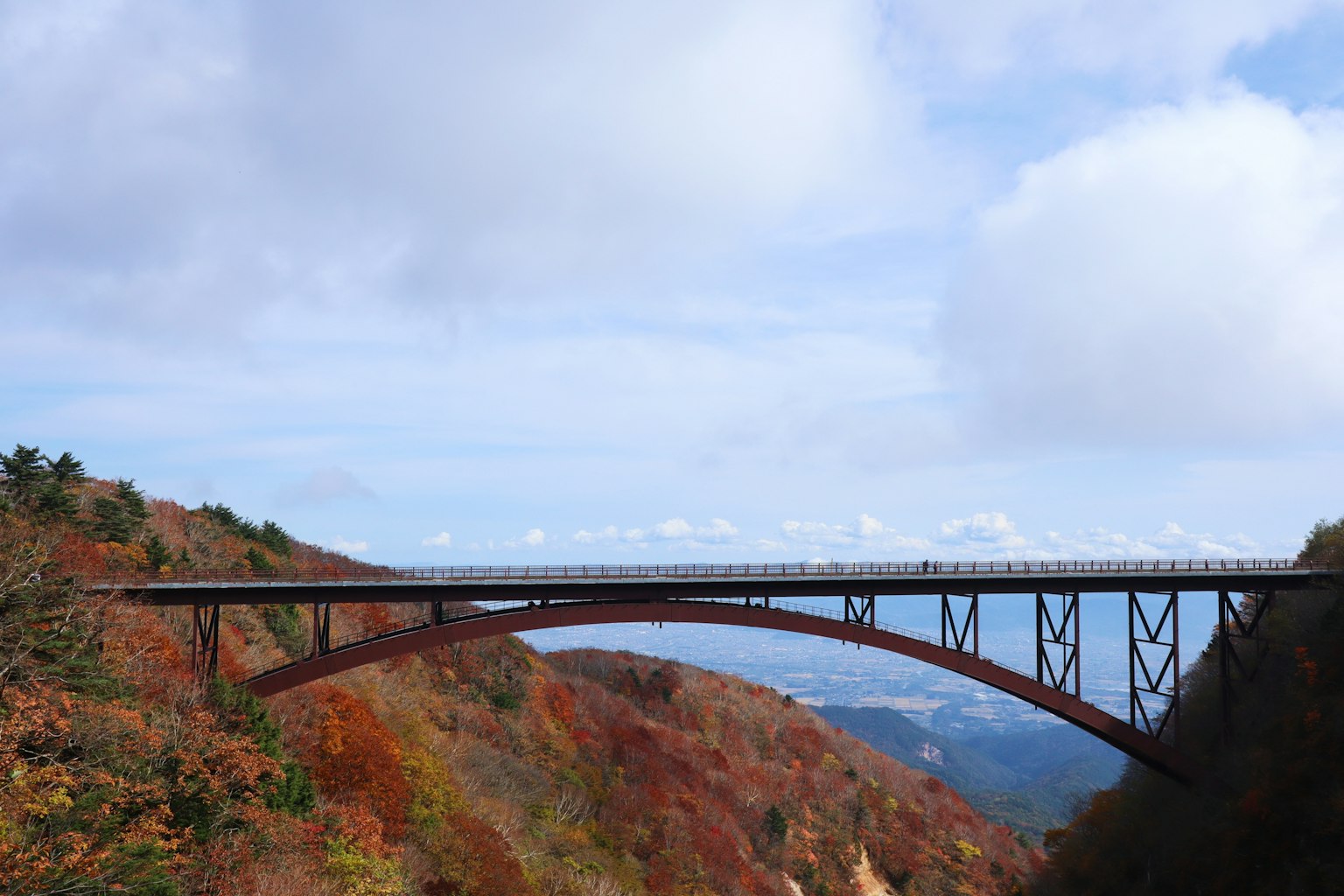 สะพานโค้งสีแดงที่มีภูเขาใบไม้ร่วงสวยงามเป็นฉากหลัง