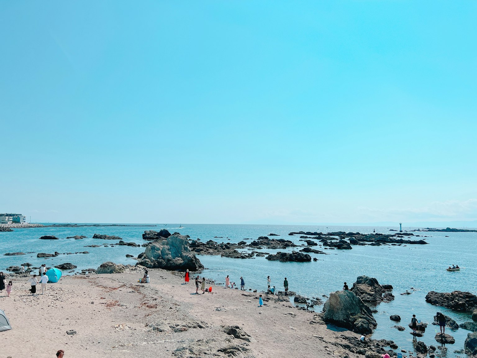 Beach scene with clear blue sky and ocean rocks and sandy shore visible