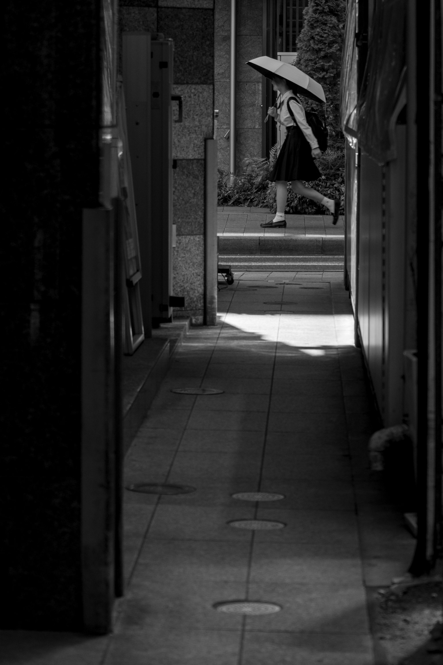 Femme marchant dans une ruelle étroite avec un parasol dans un décor en noir et blanc