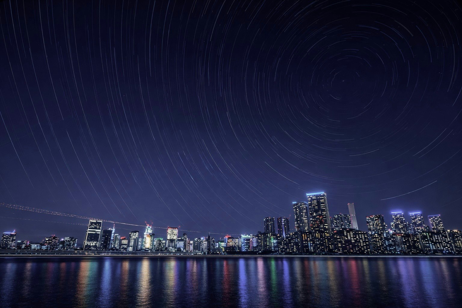 夜の川沿いに並ぶ高層ビル群と星空のような流跡