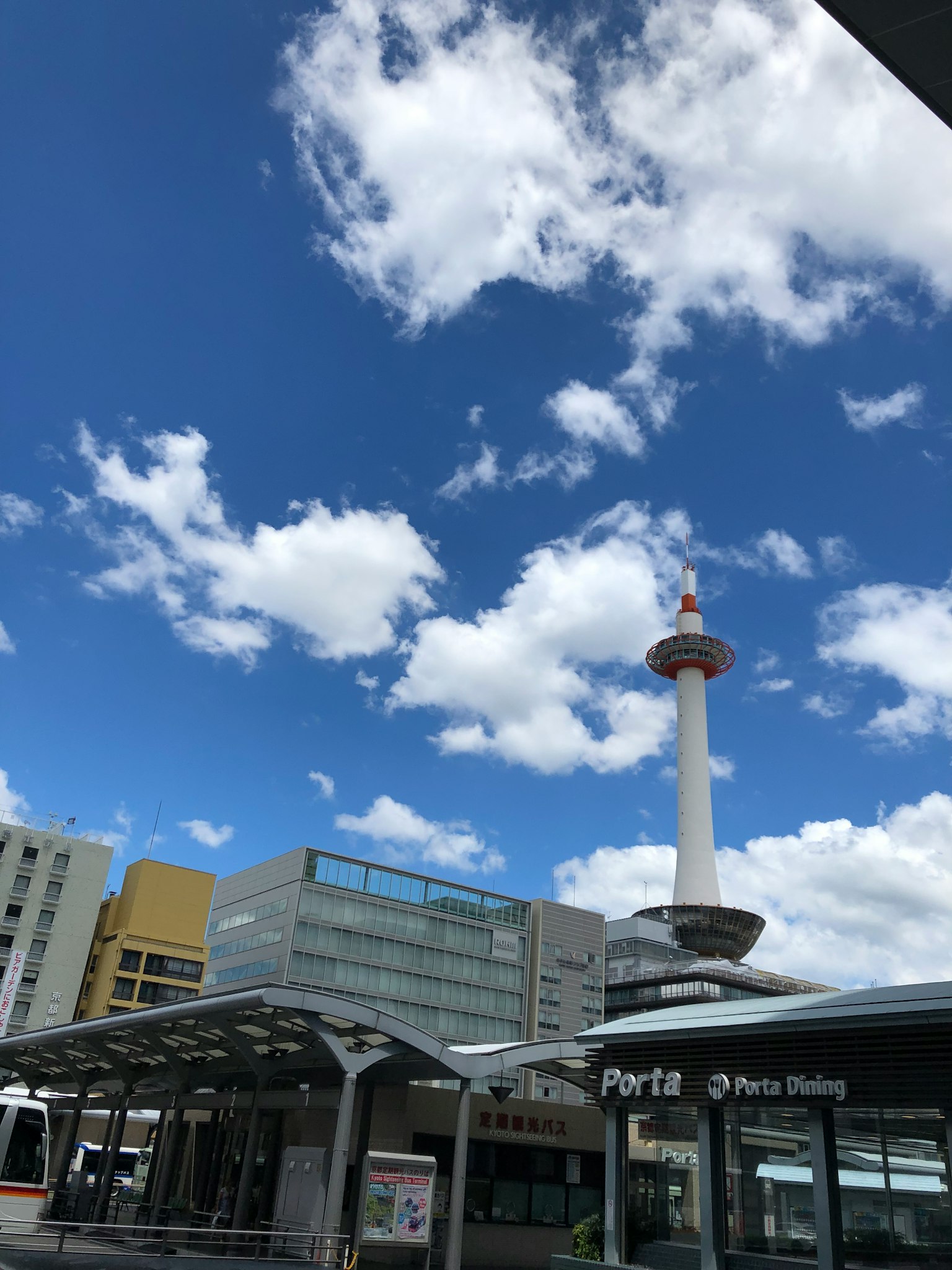 Kyoto Tower under a blue sky with clouds and nearby buildings