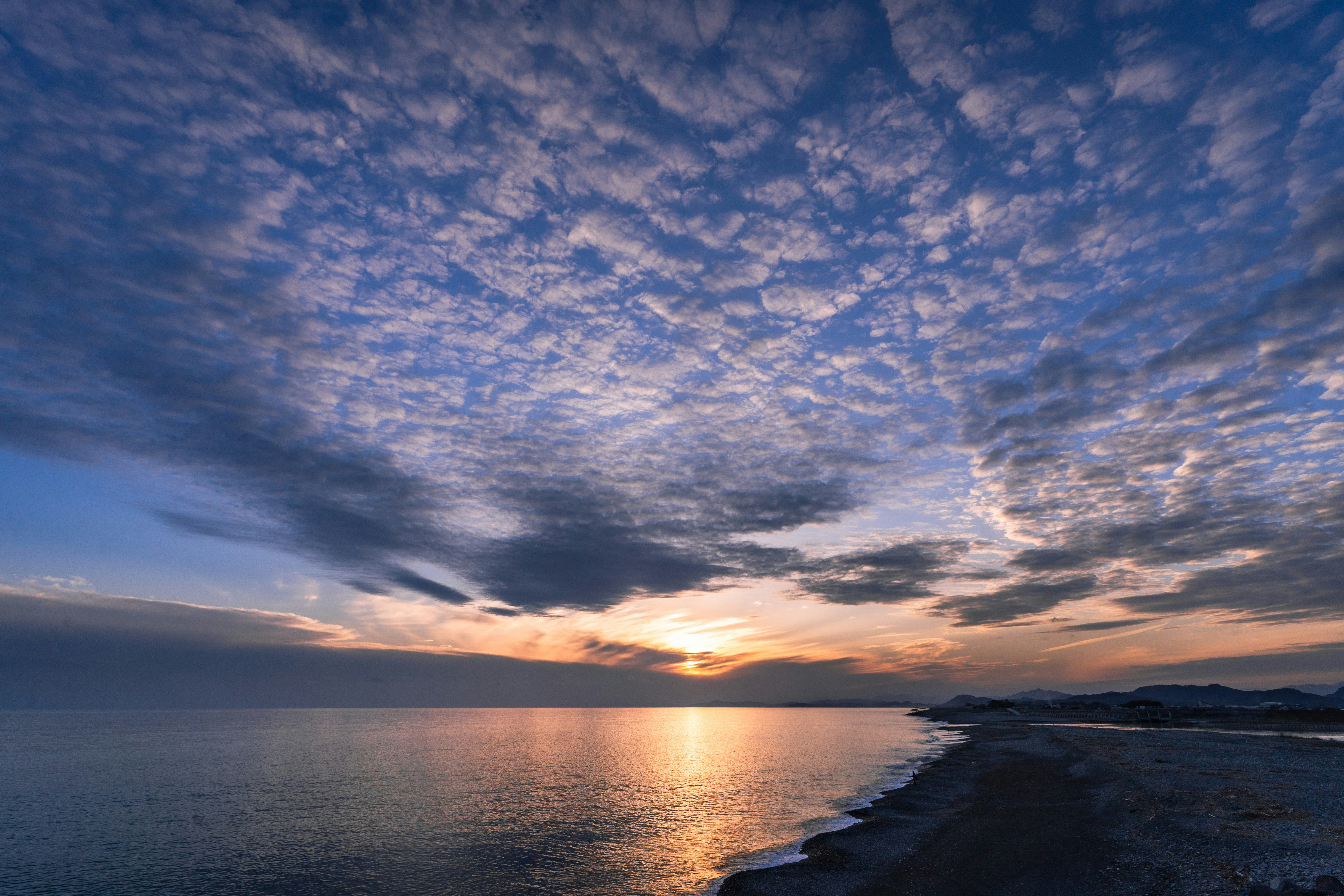 水平線に沈む夕日と海岸の波の風景