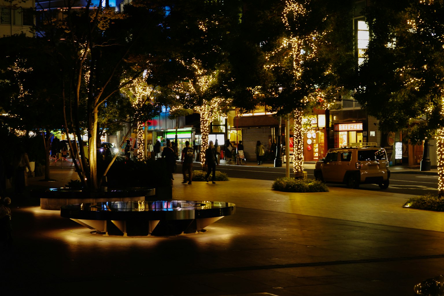 Escena nocturna de la calle iluminada por luces con personas caminando
