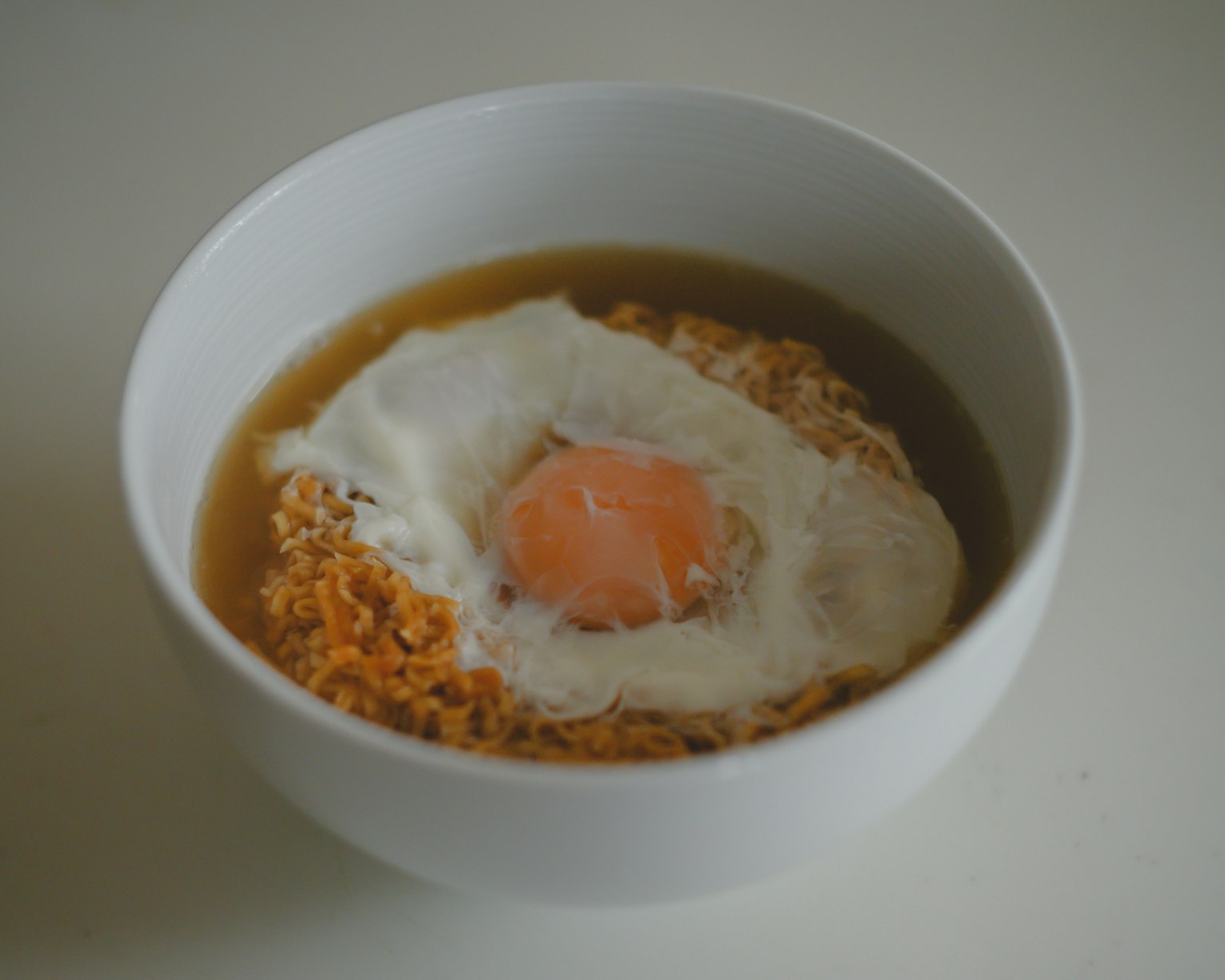 Semangkuk sup dengan telur goreng dan mie instan yang melunak