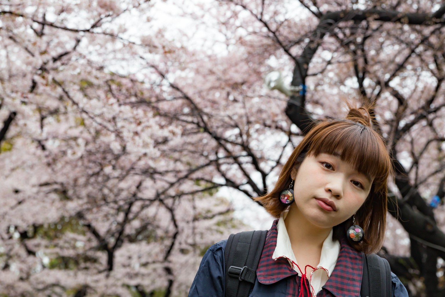 Portrait d'une femme devant des cerisiers en fleurs avec une coupe au carré et des boucles d'oreilles