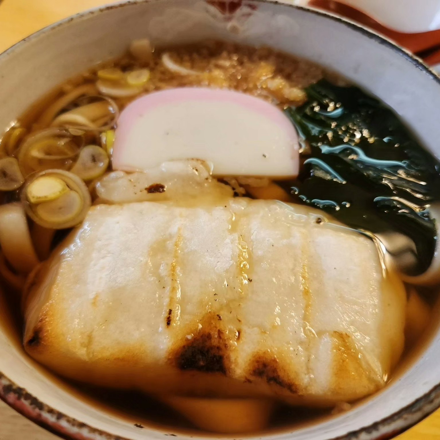 Un bol de nouilles udon avec du poisson grillé, des oignons verts et du kamaboko dans un bouillon