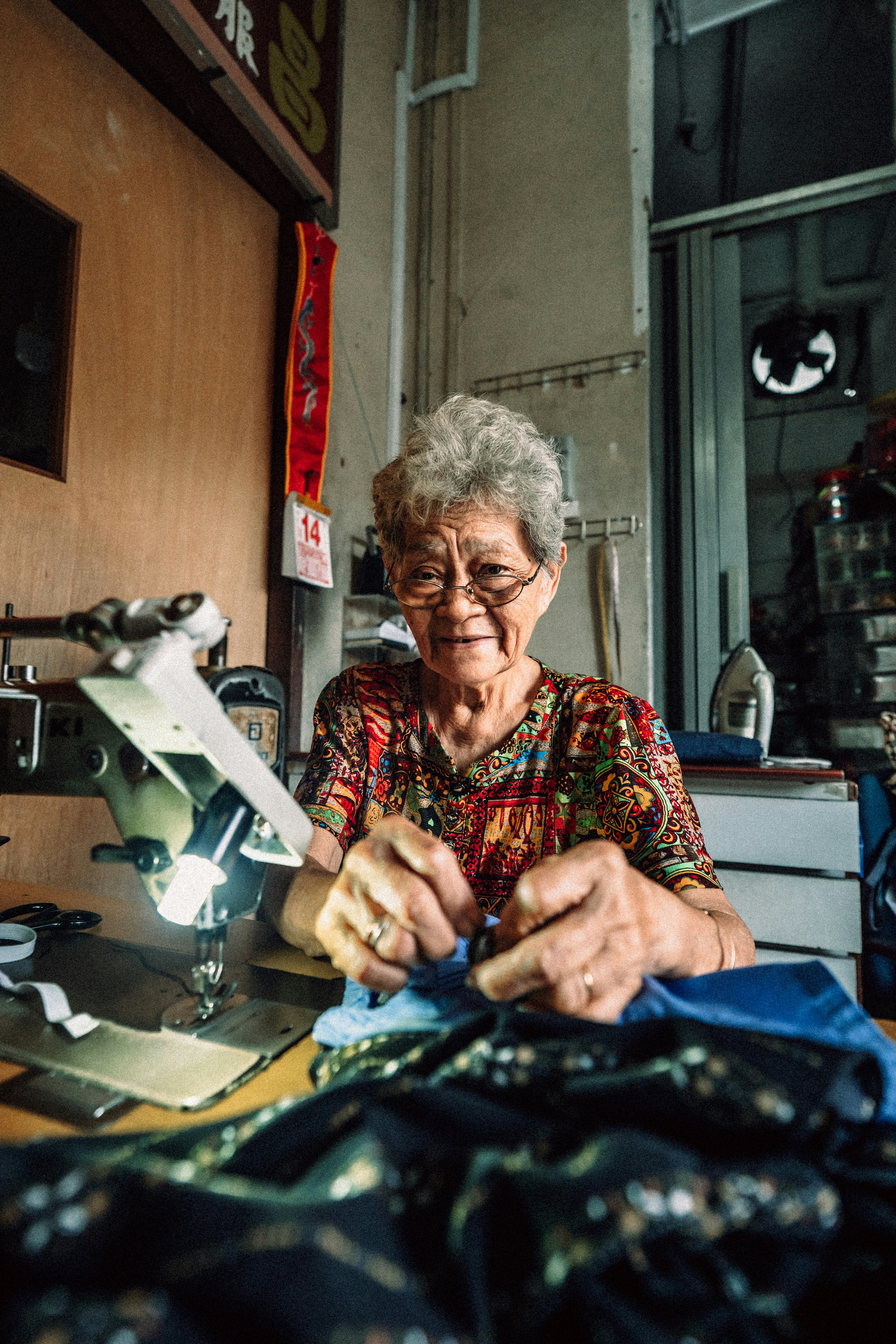 仕立て作業台の前で手元を見せる高齢の女性の工房風景