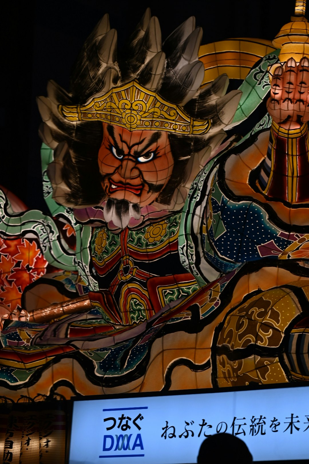 提灯と巨大な鬼の壁画が並ぶ夜の街角
