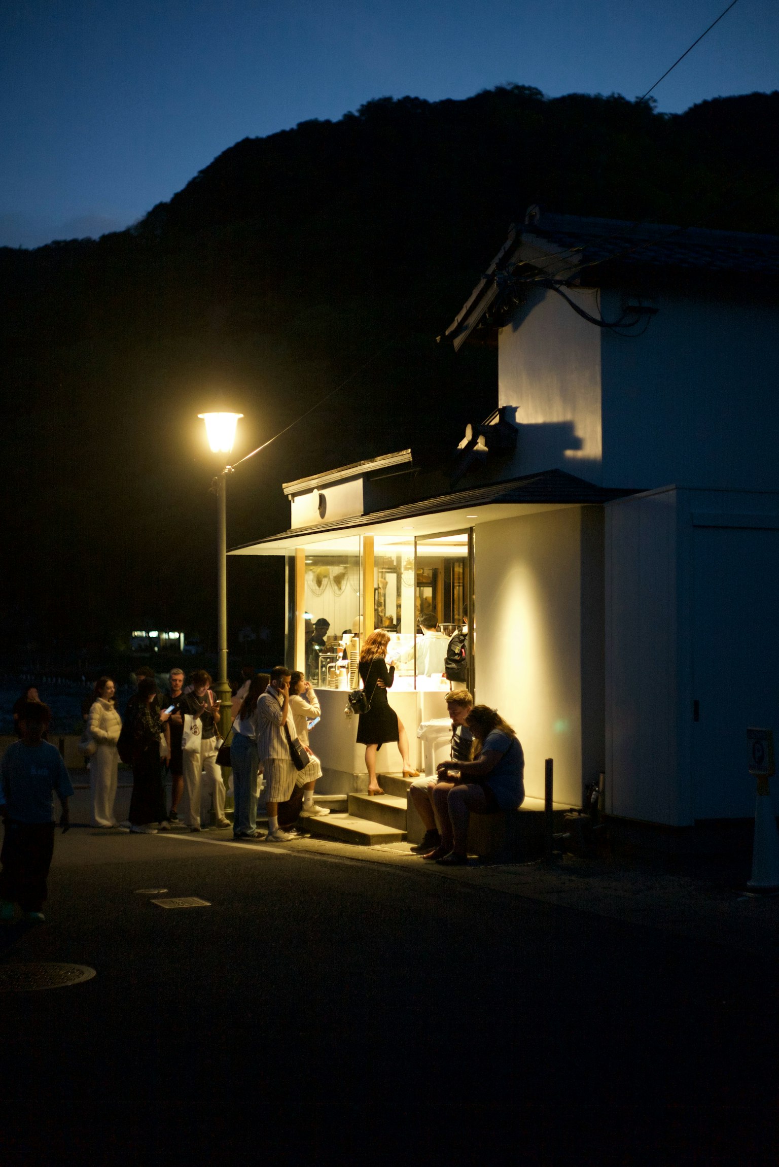 夜の街角に立つ小さな店の前に集まる人々