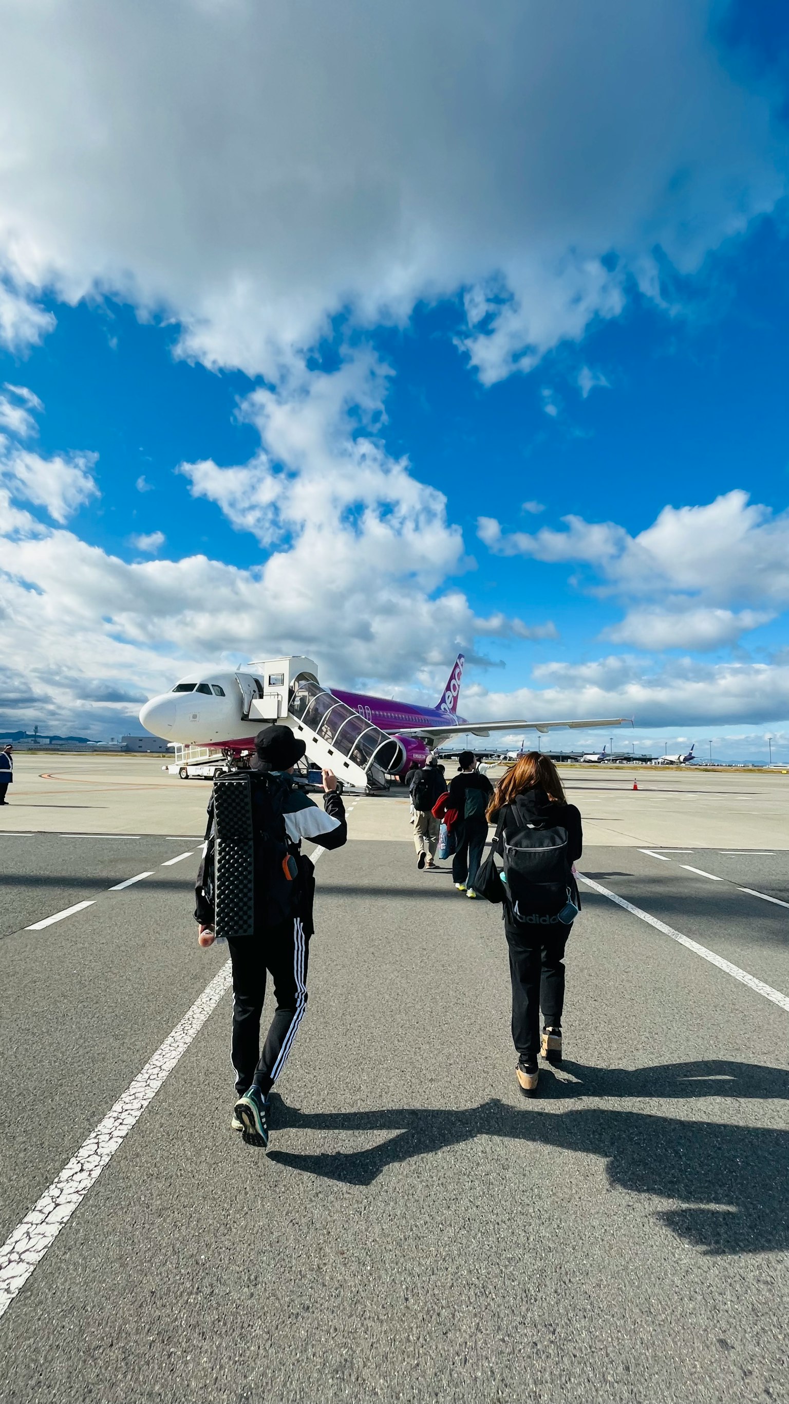 공항 활주로에서 보라색 비행기로 걸어가는 승객들