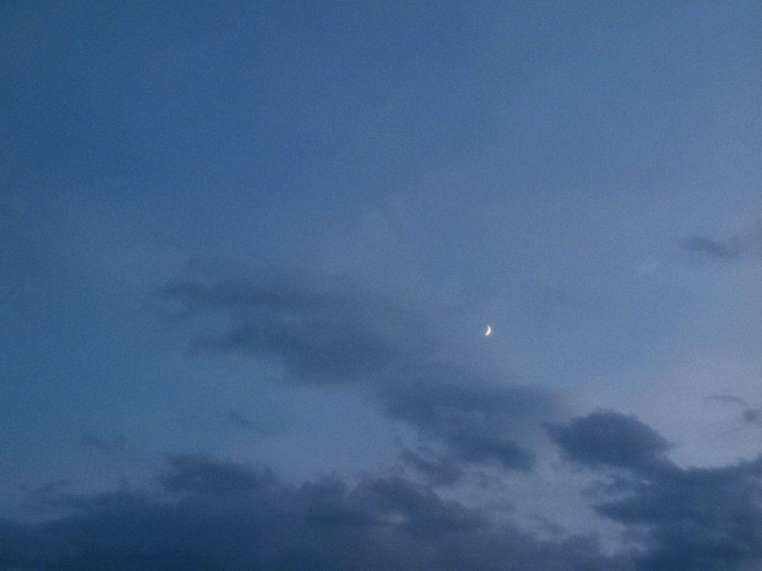 Una luna crescente luminosa in un cielo blu con nuvole morbide