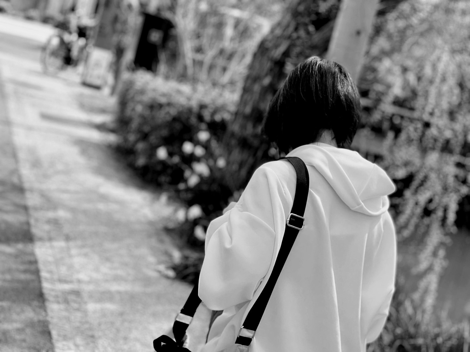 흰색 후드티를 입은 여성이 뒷모습으로 걷고 있는 흑백 사진