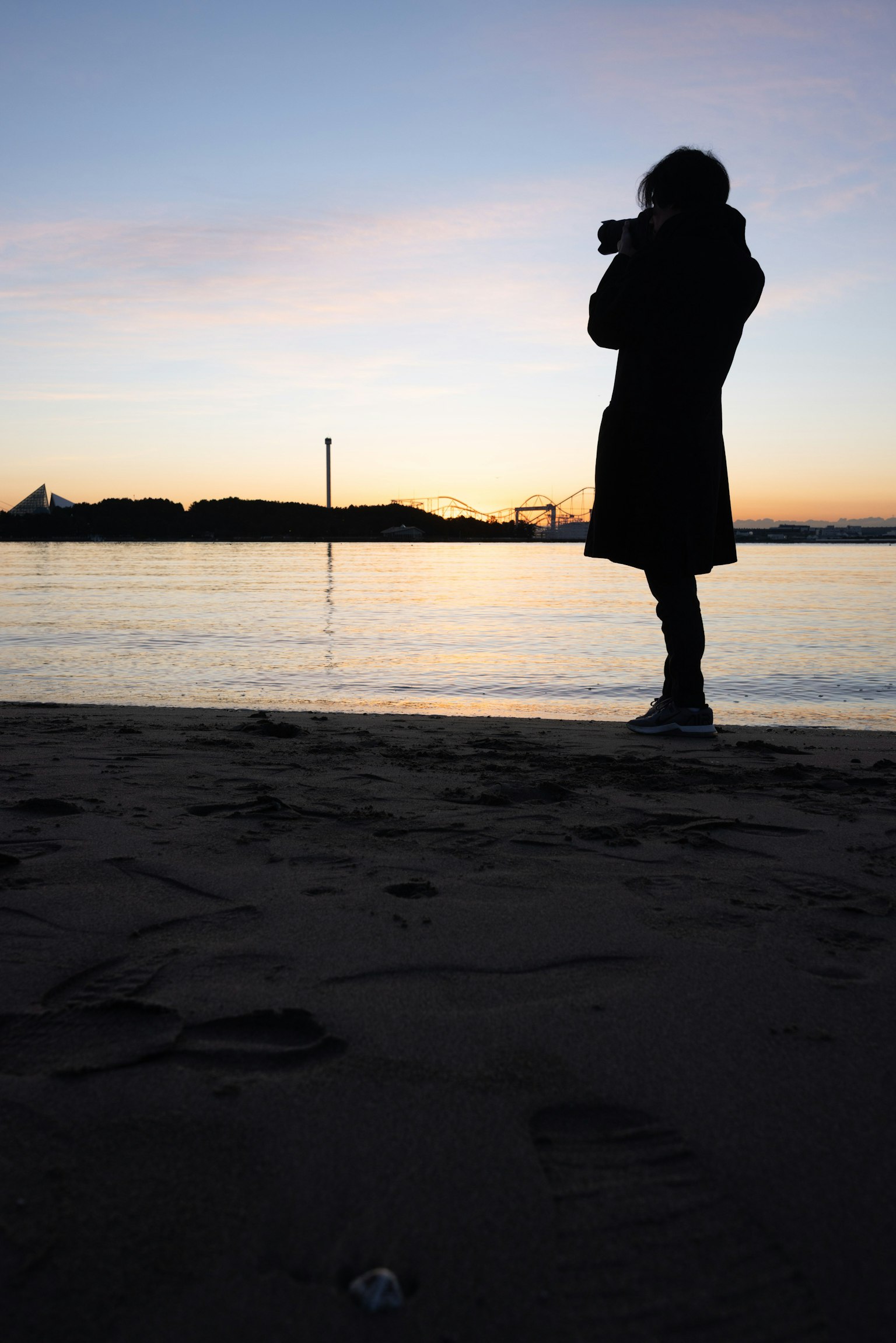 Silueta de una persona sosteniendo una cámara al atardecer junto al mar